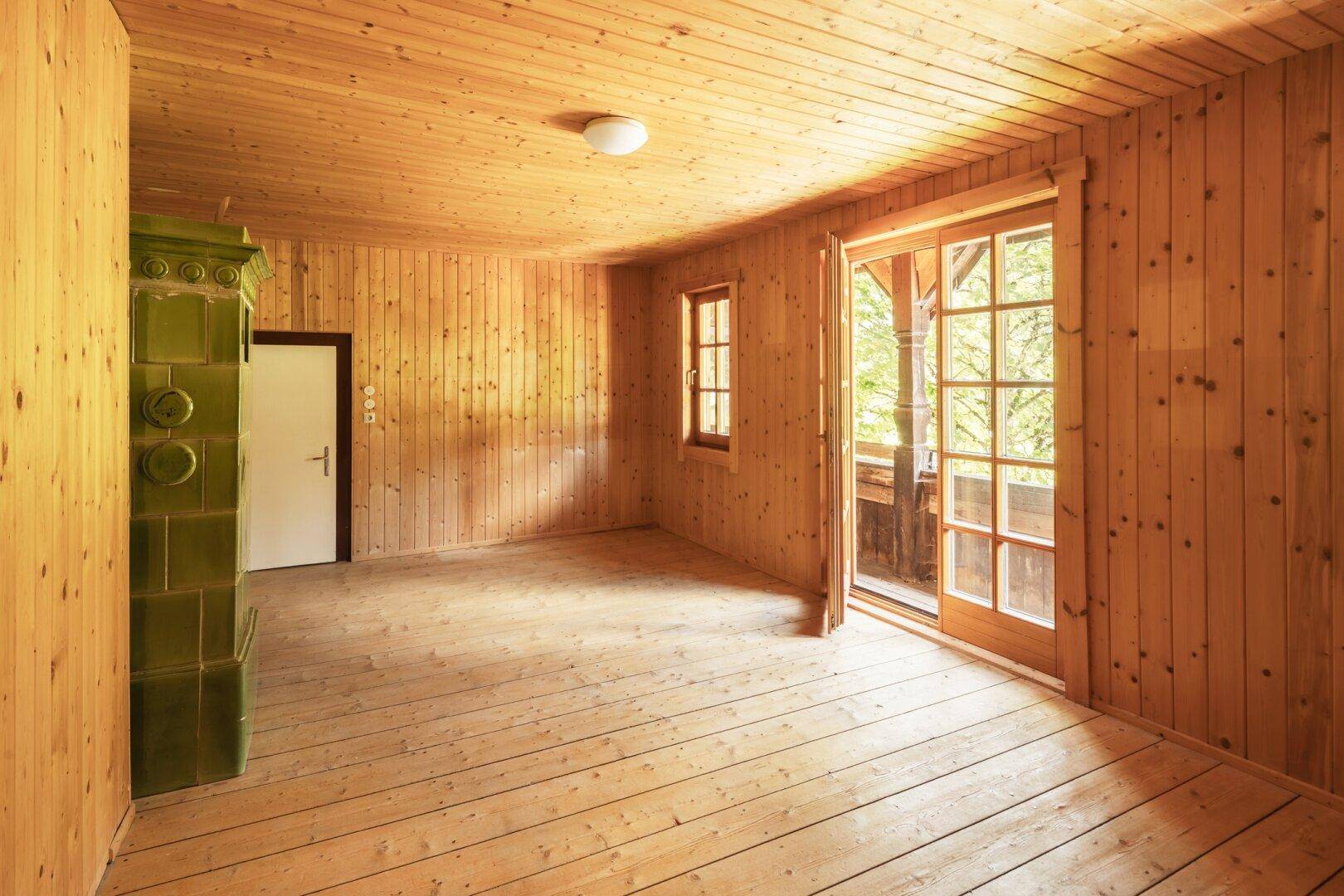 Wohnzimmer mit Holztäfelung, Holzdielenboden und direktem Zugang zum Balkon.