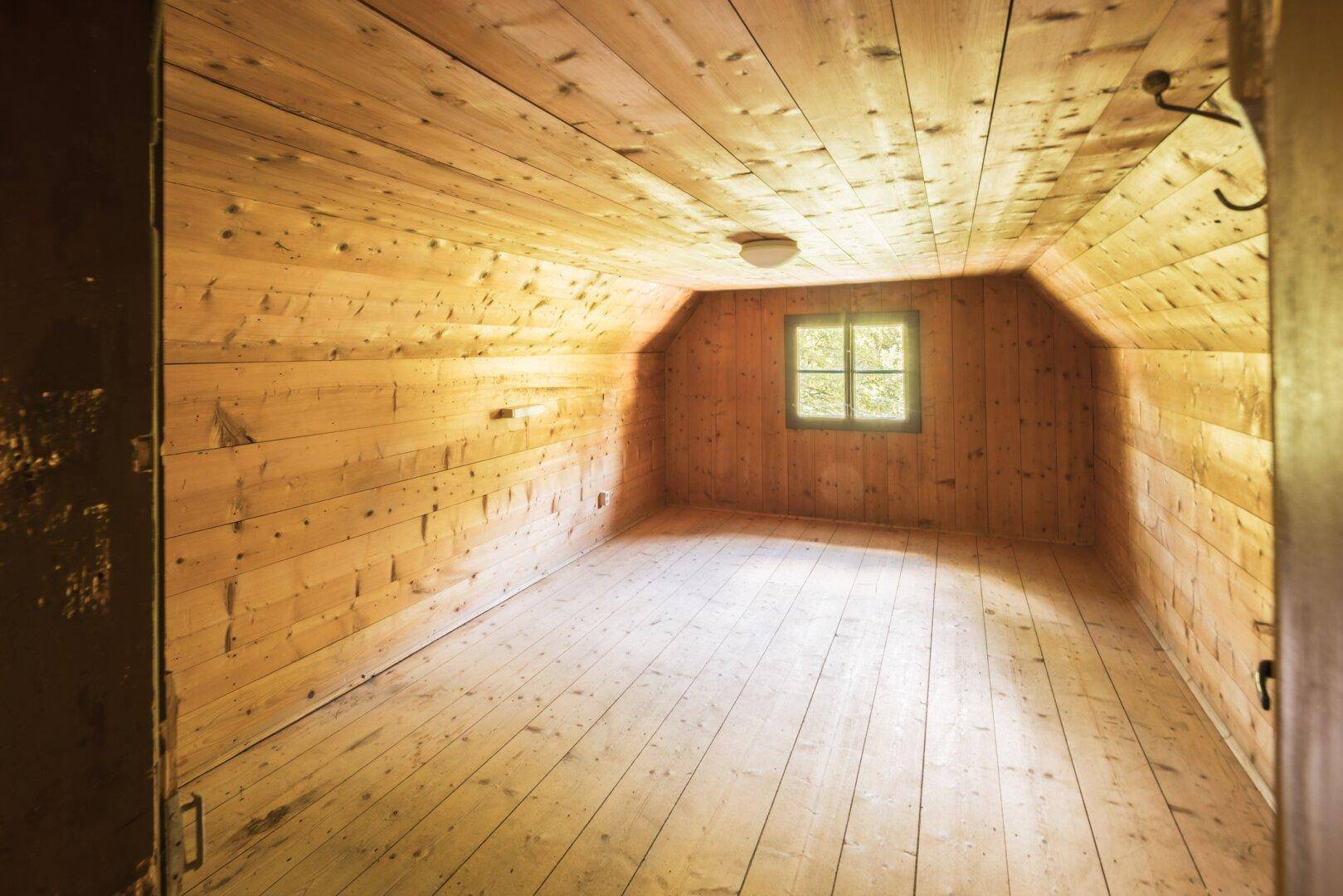 Dachgeschosszimmer mit Holztäfelung, Holzdielenboden und einem kleinen Fenster.