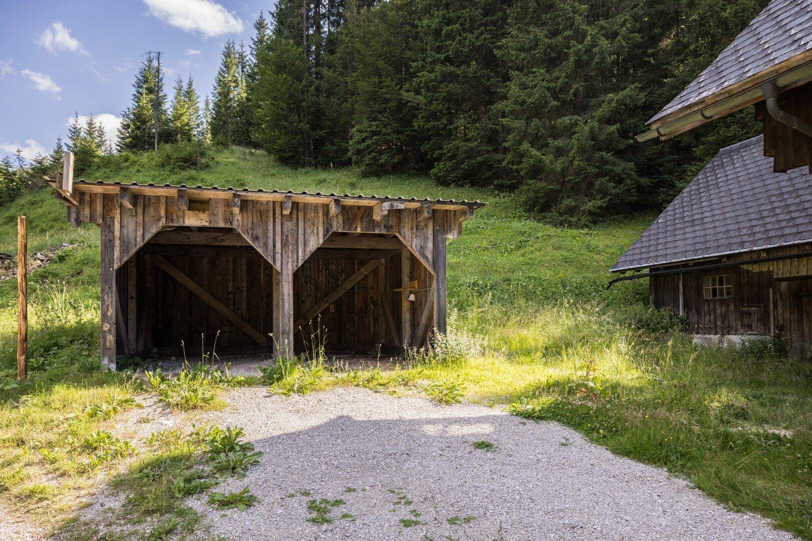 Offener Holzunterstand oder Carport neben dem Haupthaus in ländlicher Umgebung.