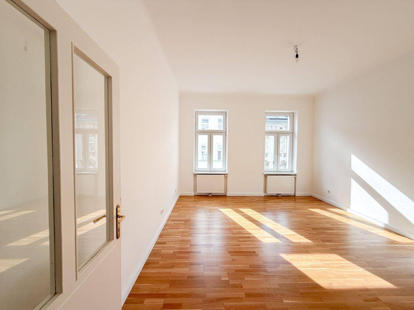 Heller Wohnbereich mit Holzboden und weiß gestrichenen Wänden, bereit zur individuellen Gestaltung.
