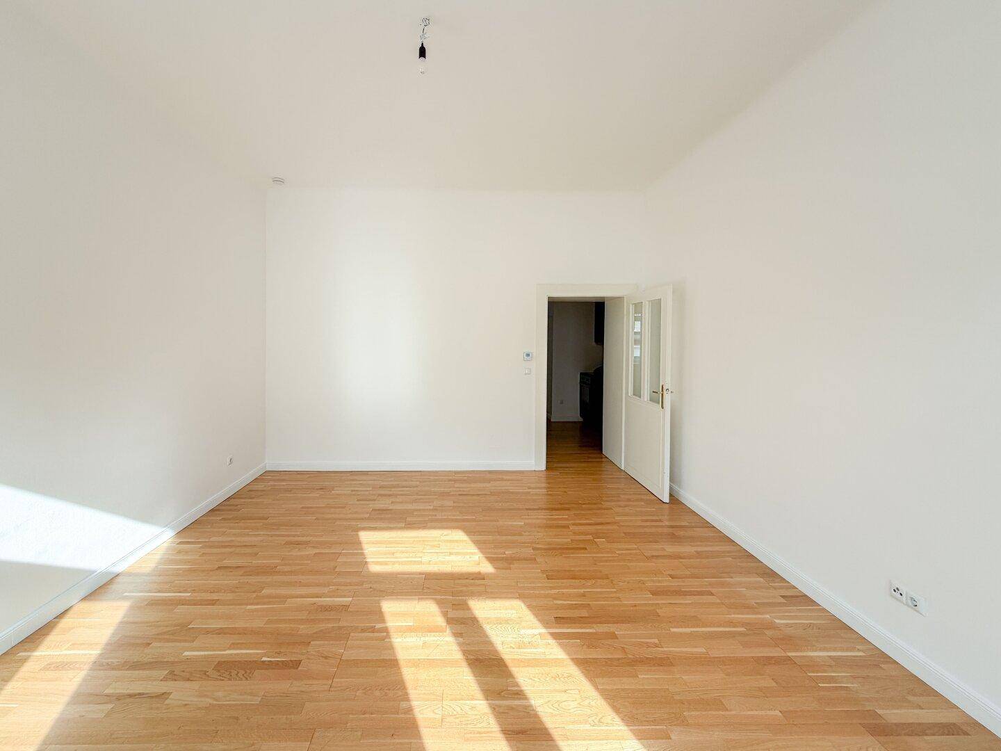 Heller Wohnbereich mit Holzboden und offenem Zugang zu einem weiteren Raum, ideal für flexible Nutzung.