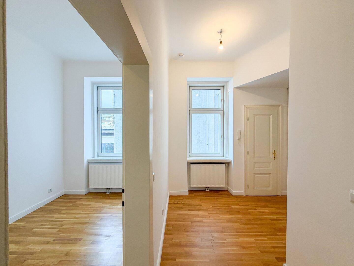 Langer Flur mit Holzboden, der zu verschiedenen hellen Räumen mit großen Fenstern führt.