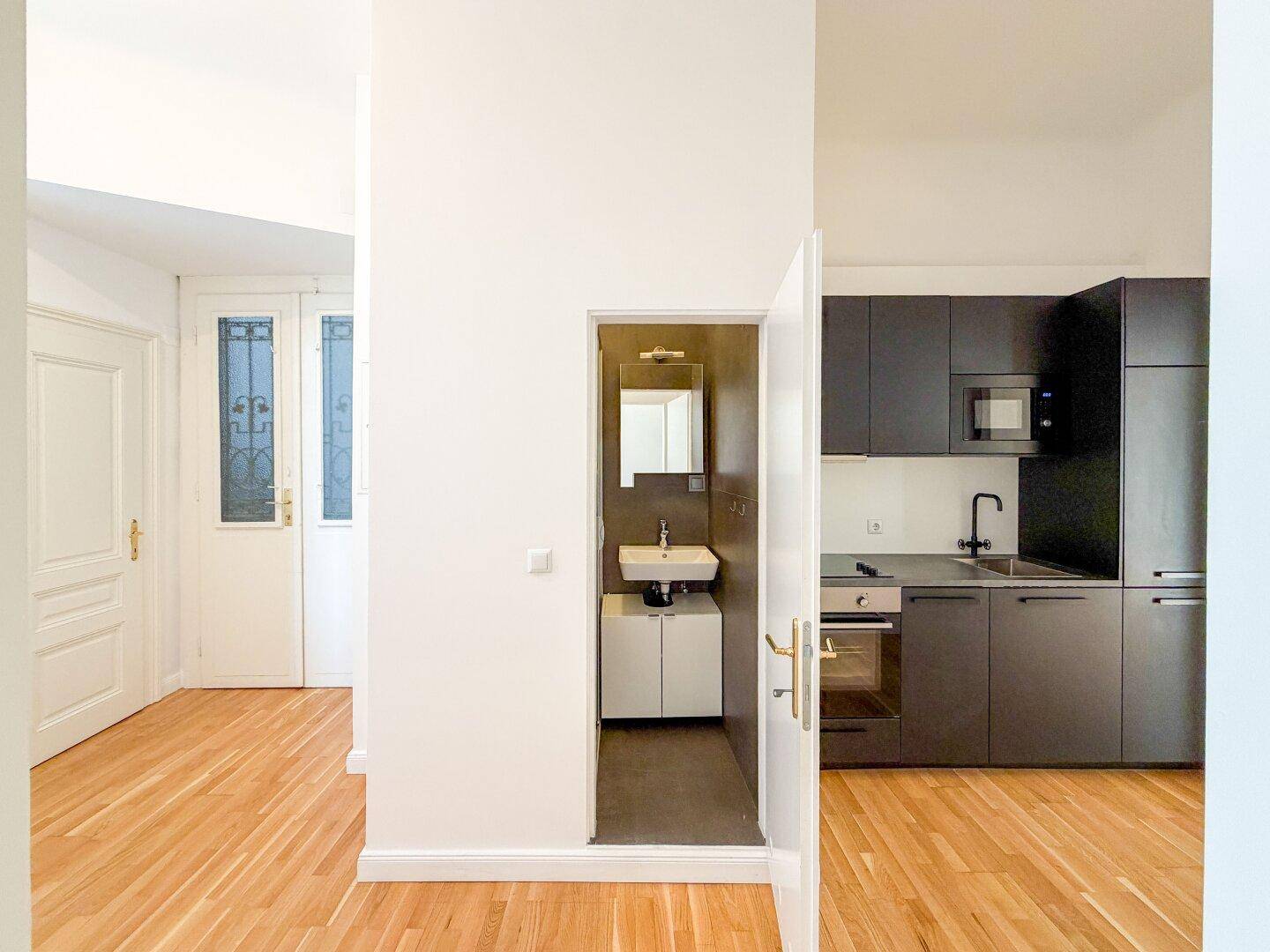 Moderne Küchenzeile in dunklem Design mit integrierten Geräten, neben einem kleinen Badezimmer.