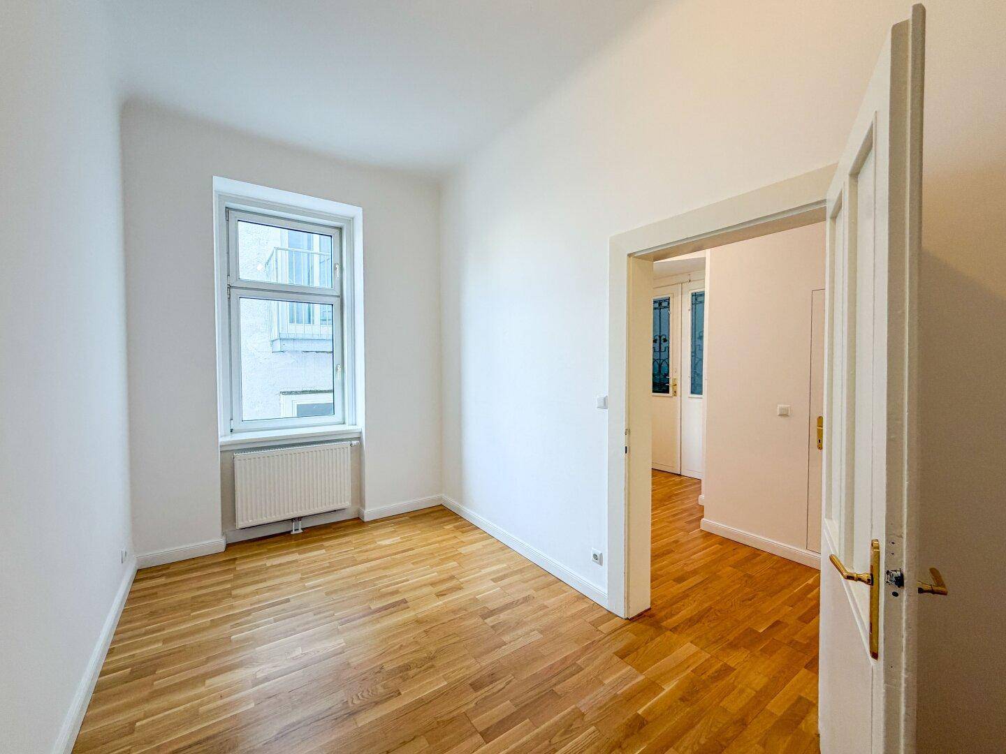 Helles Schlafzimmer mit Holzboden und einem Fenster, das den Raum mit Tageslicht füllt.