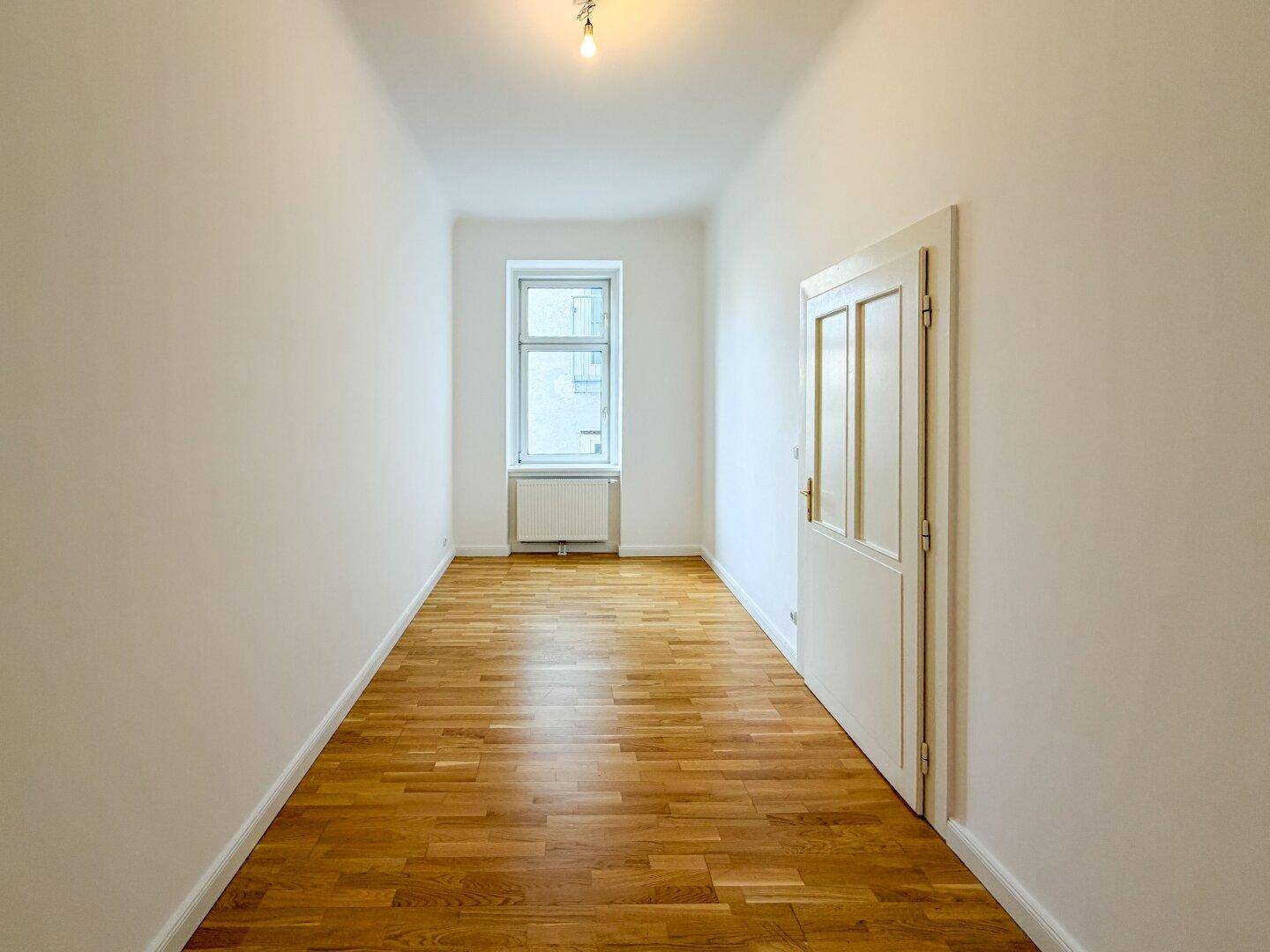Langes, schmales Schlafzimmer mit Holzboden und einem Fenster am Ende des Raumes.