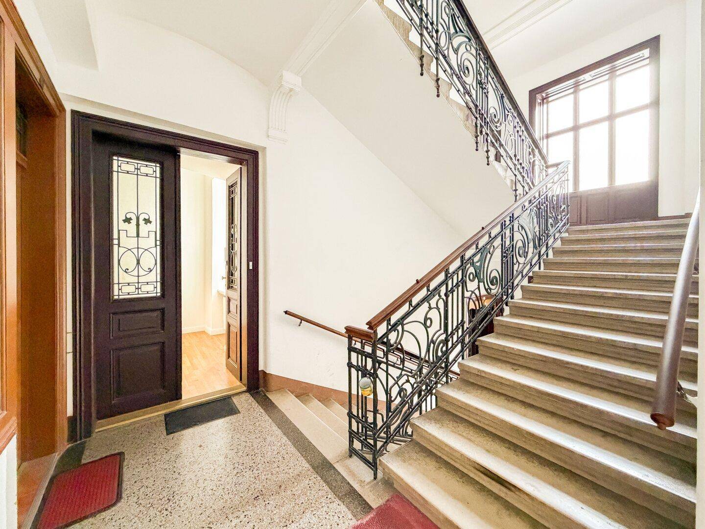 Historisches Treppenhaus mit schmiedeeisernem Geländer und Terrazzoboden, typisch für Altbauten.
