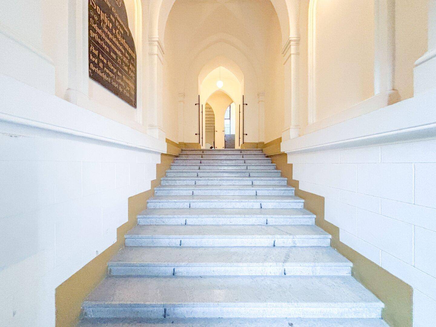 Repräsentatives Treppenhaus mit Steinstufen und hohen Gewölbedecken in einem Altbau.