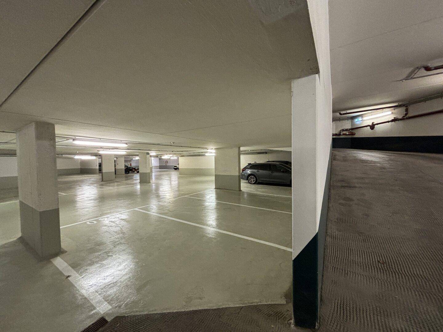 Weitläufige Tiefgarage mit vielen Stellplätzen und einer breiten Zufahrtsrampe für Fahrzeuge.
