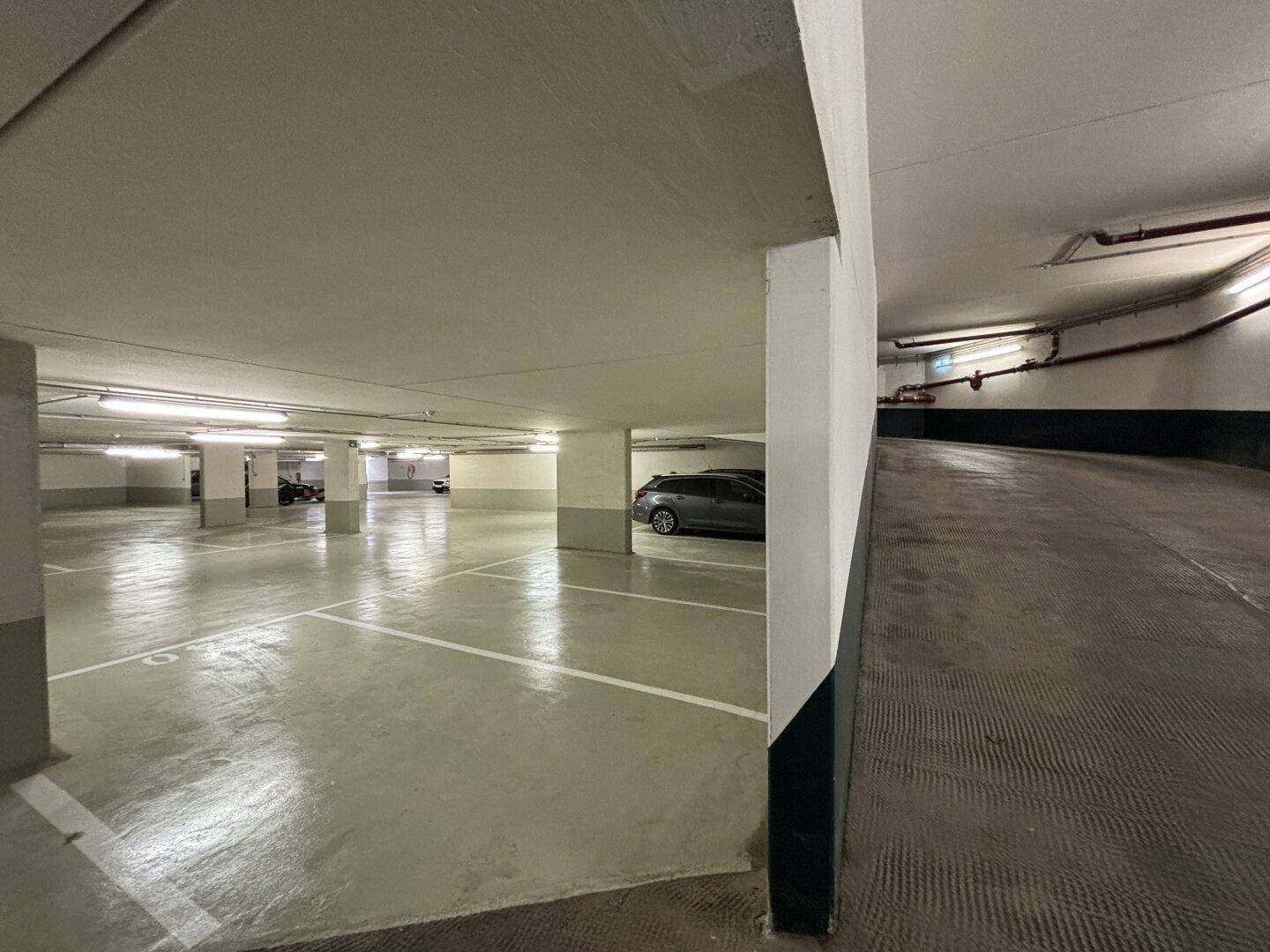 Blick in die Tiefgarage mit Stellplätzen und der Zufahrtsrampe, die nach oben führt.