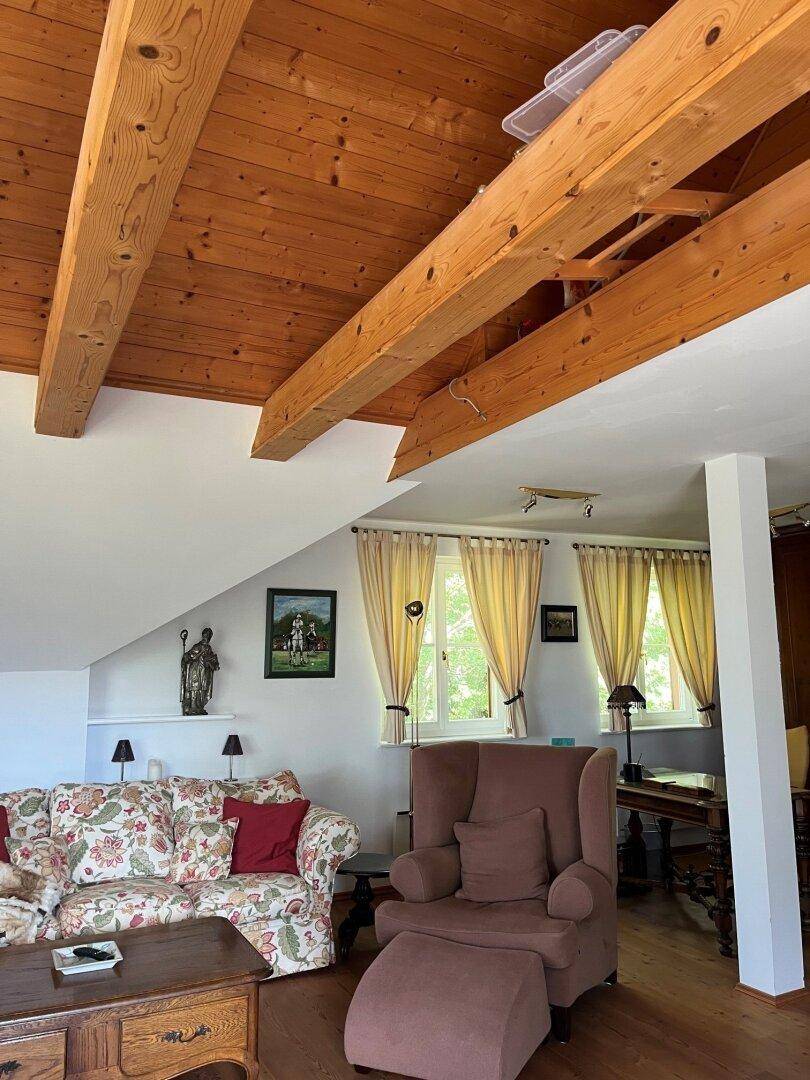 Gemütliches Wohnzimmer mit Holzbalkendecke, traditionellen Möbeln und Fenstern.