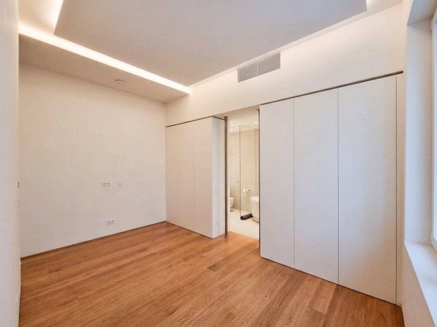 Schlafzimmer mit Holzboden und Schiebetüren, die zu einem modernen Bad mit Dusche führen.