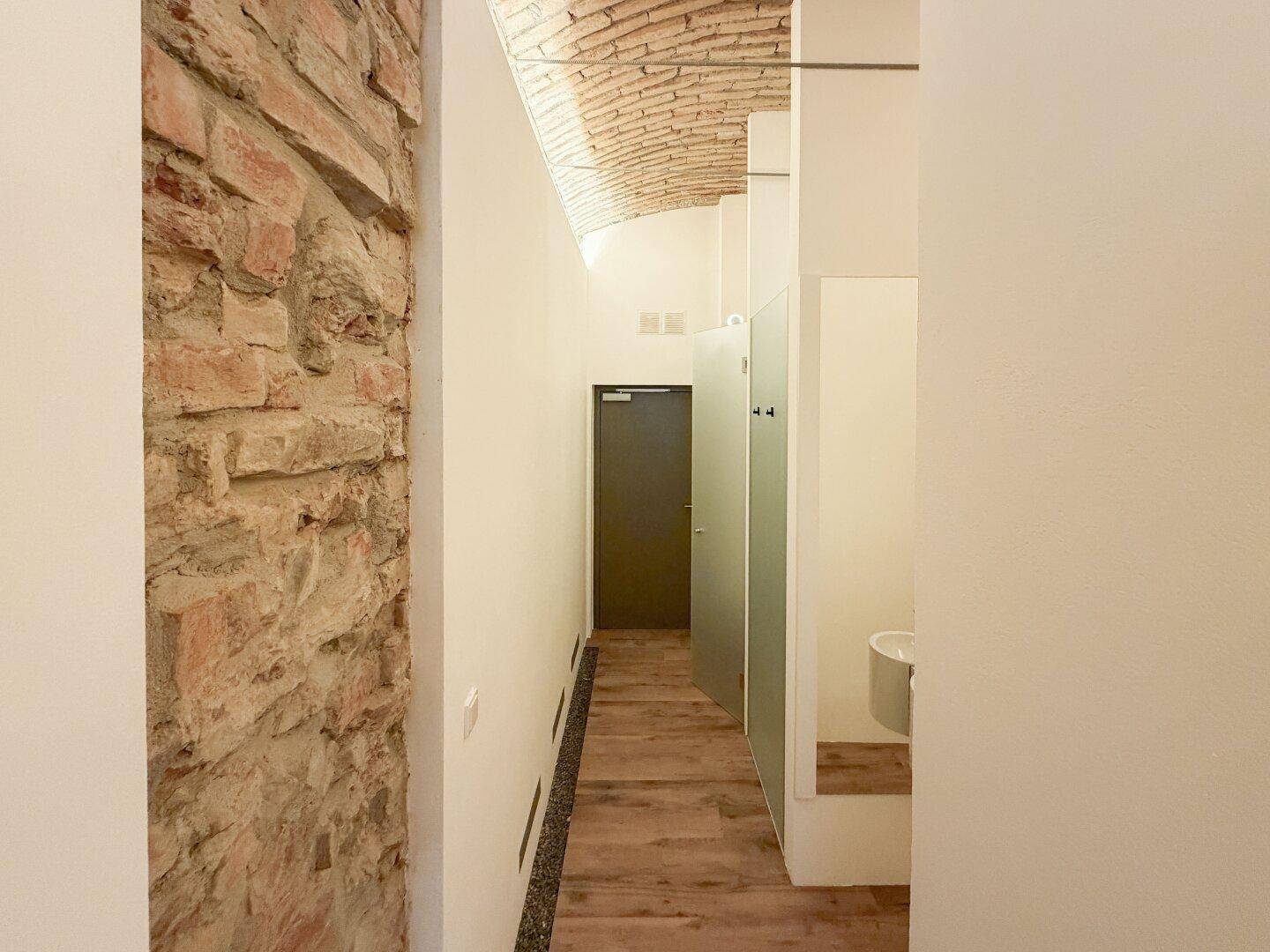 Heller Flur mit Holzboden, freiliegender Ziegelwand und modernen Milchglas-Trennwänden.
