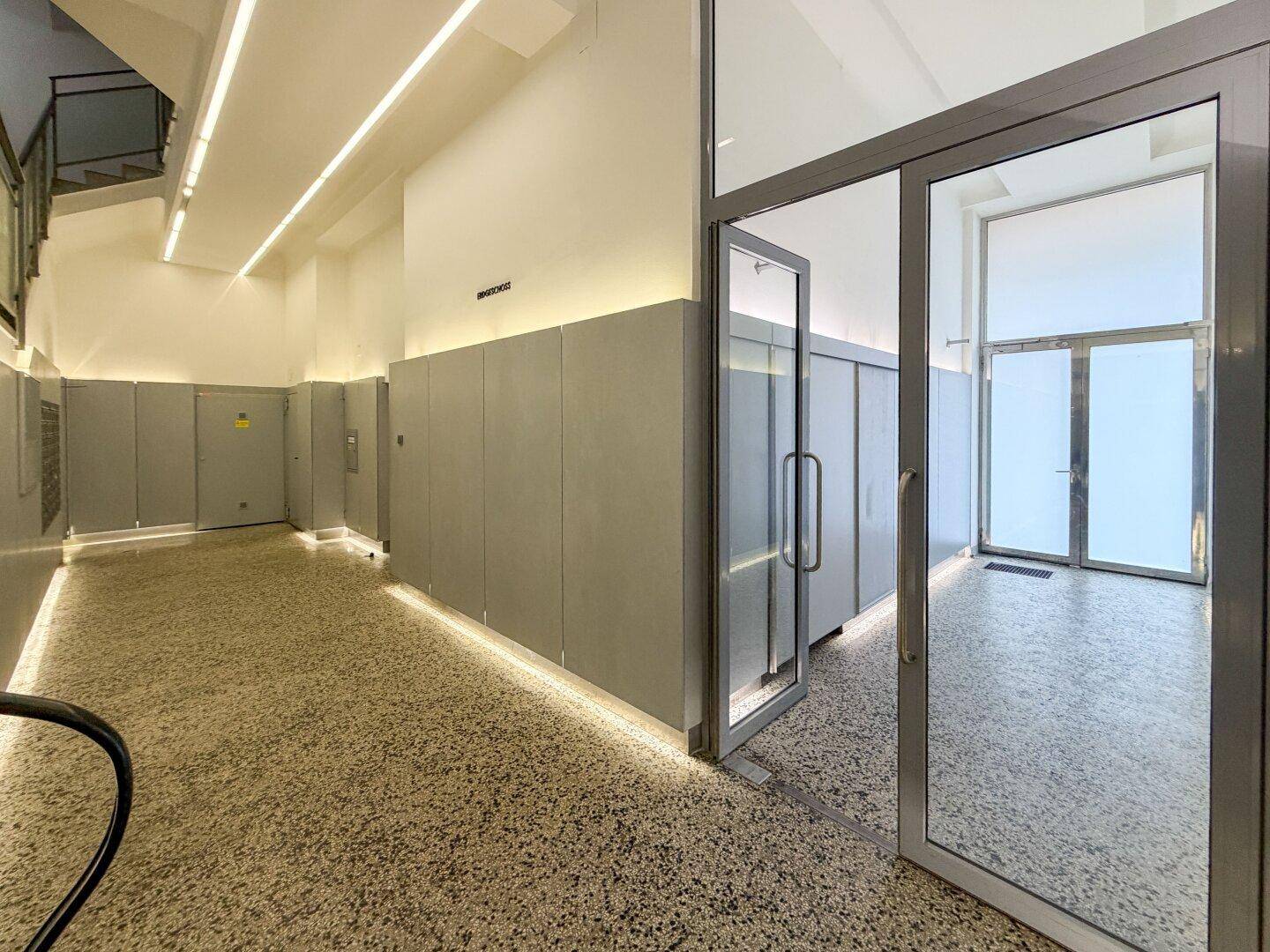 Moderner Eingangsbereich mit Terrazzoboden, Glas- und Metalltüren sowie indirekter Beleuchtung und Aufzugzugang.