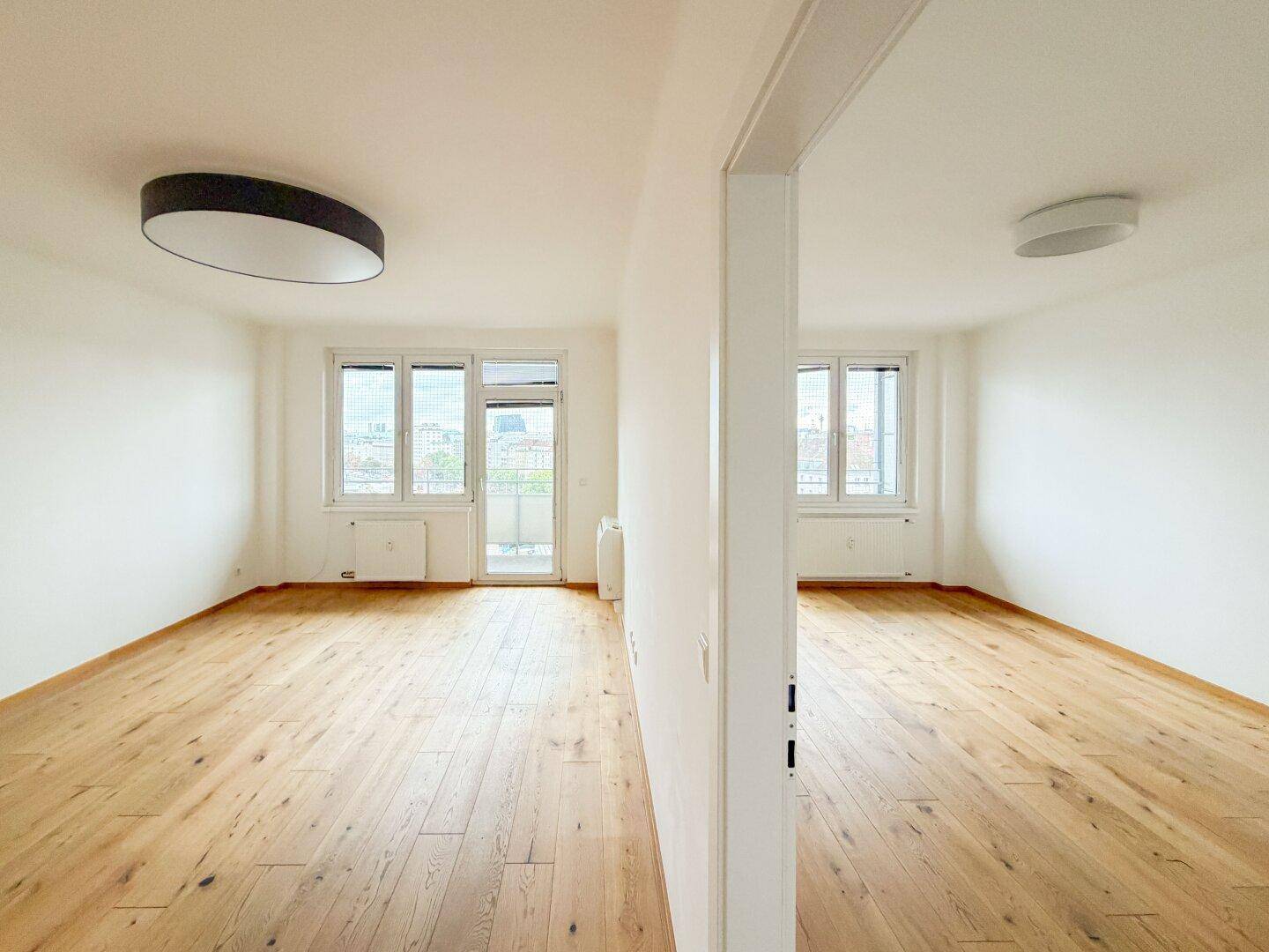 Zwei helle, miteinander verbundene Räume mit Eichenparkett, ideal für einen offenen Wohn-Essbereich.