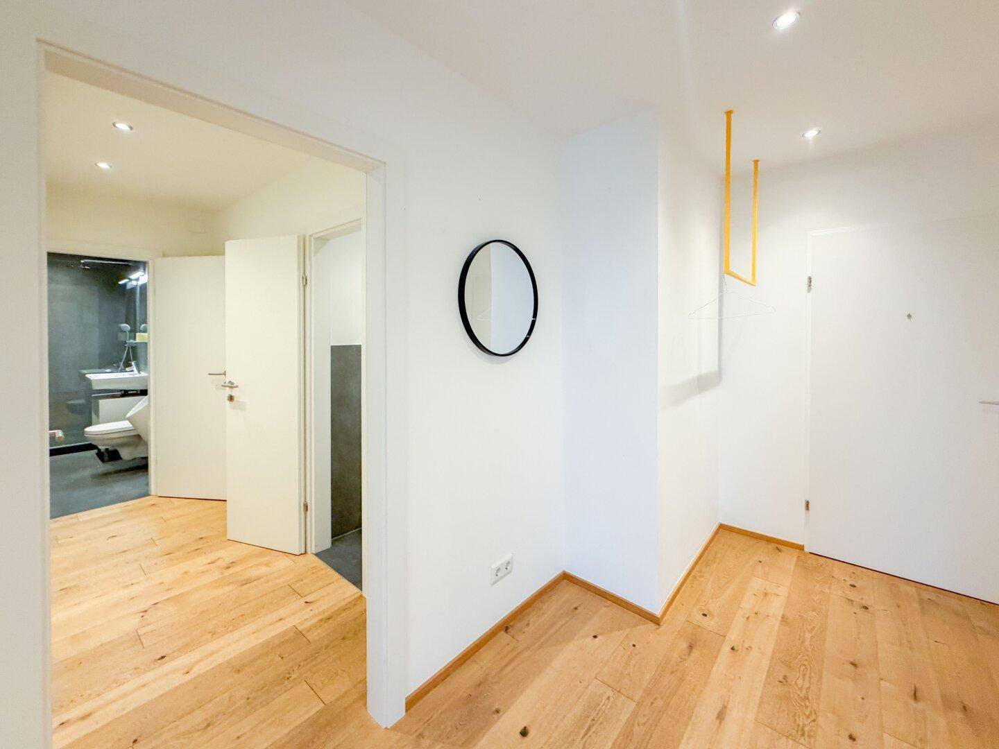 Heller Flur mit Holzparkettboden, der zu einem modernen Badezimmer und einer Gästetoilette führt.