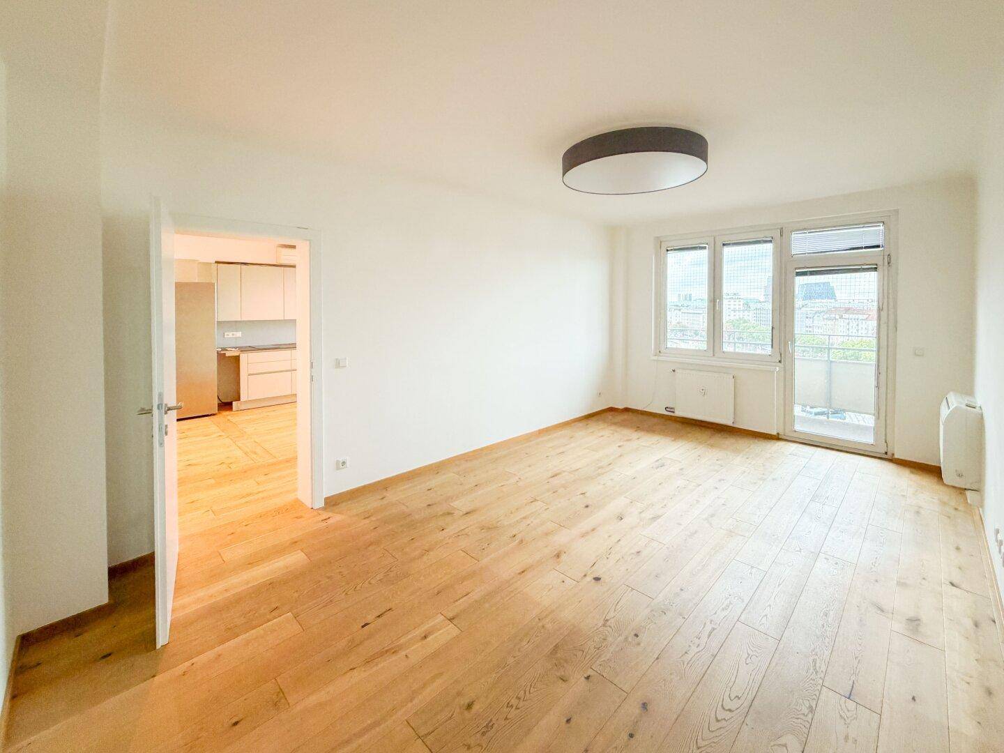 Geräumiges Wohnzimmer mit Holzparkettboden und Blick in die angrenzende, moderne Küchenzeile.