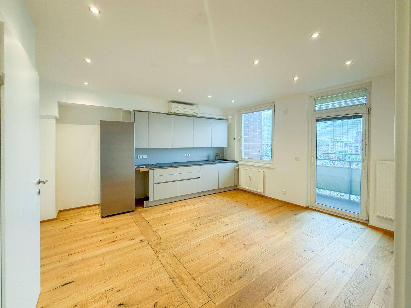 Moderne Küche mit grauen Schränken, Edelstahlkühlschrank und Holzparkettboden, mit Balkonzugang.