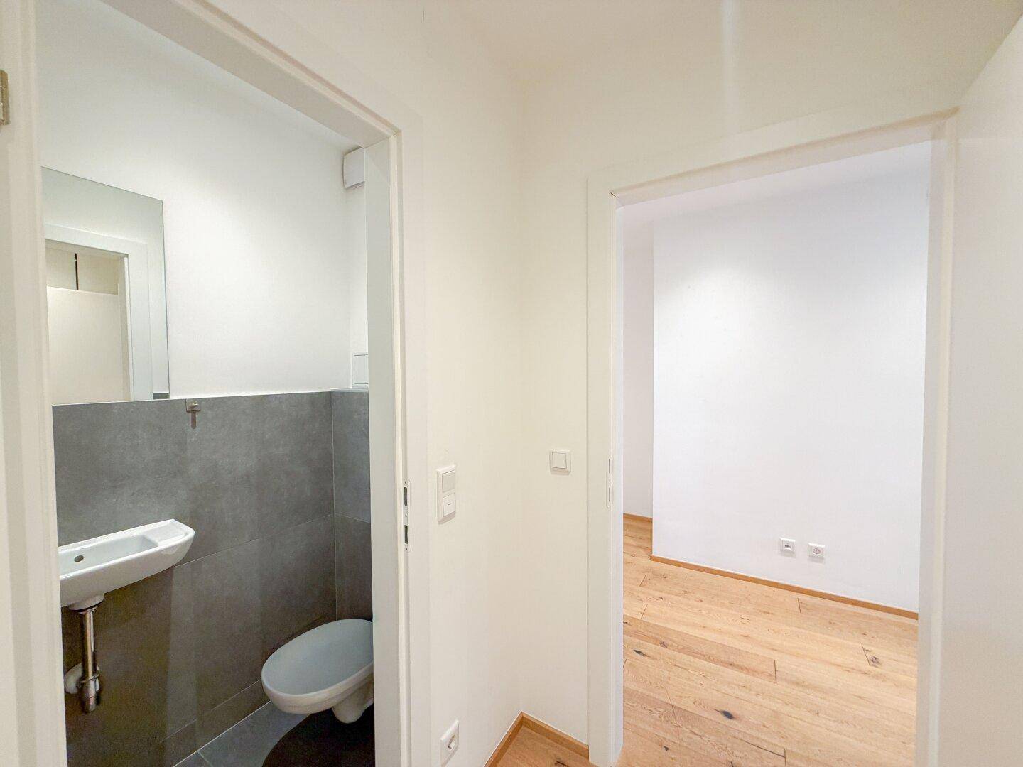 Moderne Gästetoilette mit Wand-WC, kleinem Waschbecken und grauen Fliesen im unteren Bereich.