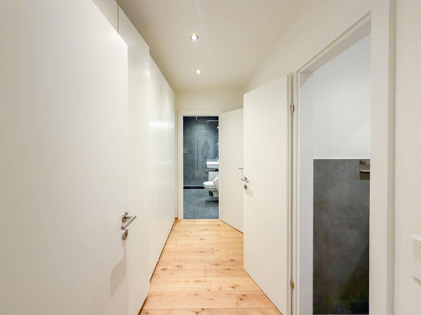 Heller Flur mit Holzparkettboden, der zu einem modernen Badezimmer und einer separaten Gästetoilette führt.