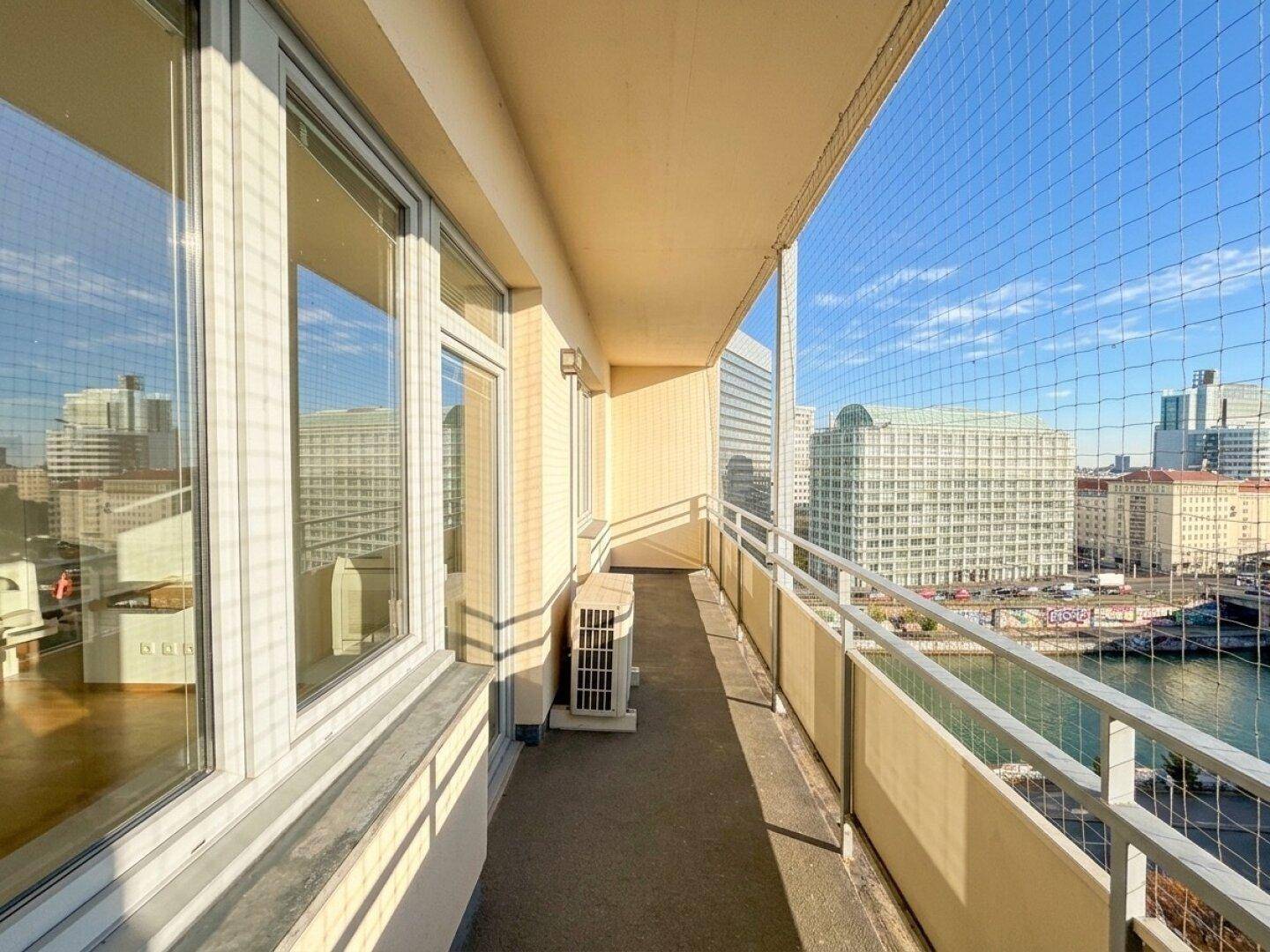 Heller Balkon mit Sicherheitsnetz und weitem Blick über die Stadt und die umliegenden Gebäude.