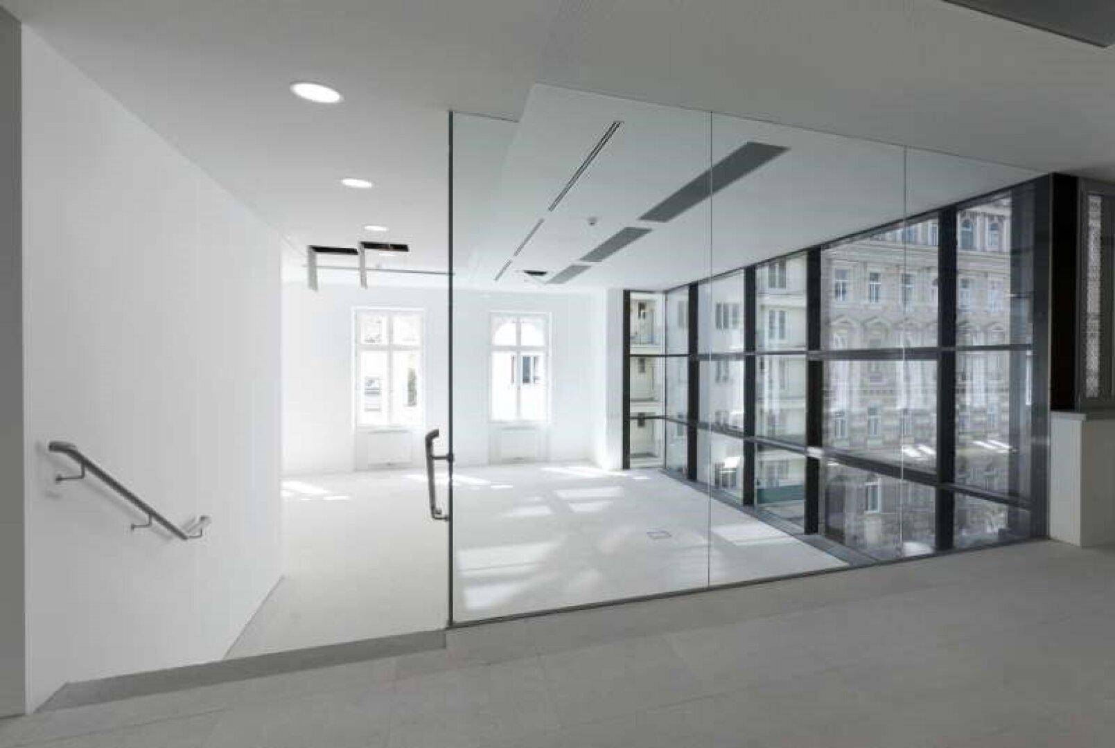 Heller, moderner Bürobereich mit großen Fenstern, Glaswänden und Blick auf die Stadt.
