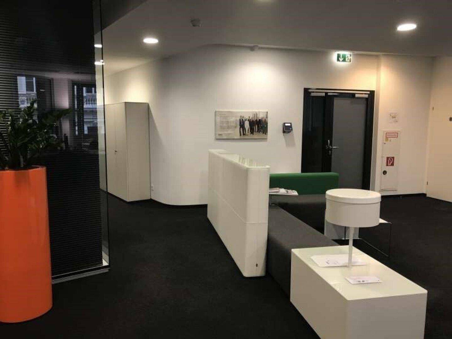 Empfangsbereich im Büro mit moderner Sitzgelegenheit, Pflanzen und dunklem Teppichboden.