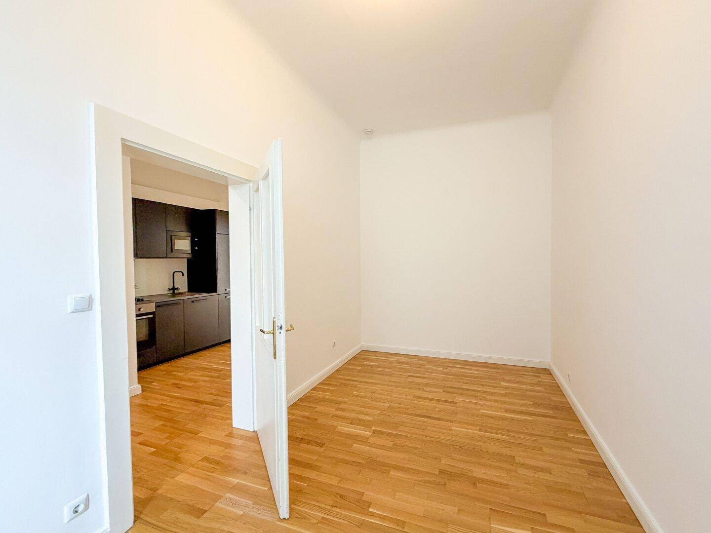Schlafzimmer mit Holzboden und offenem Zugang zur modernen Küchenzeile im Hintergrund.