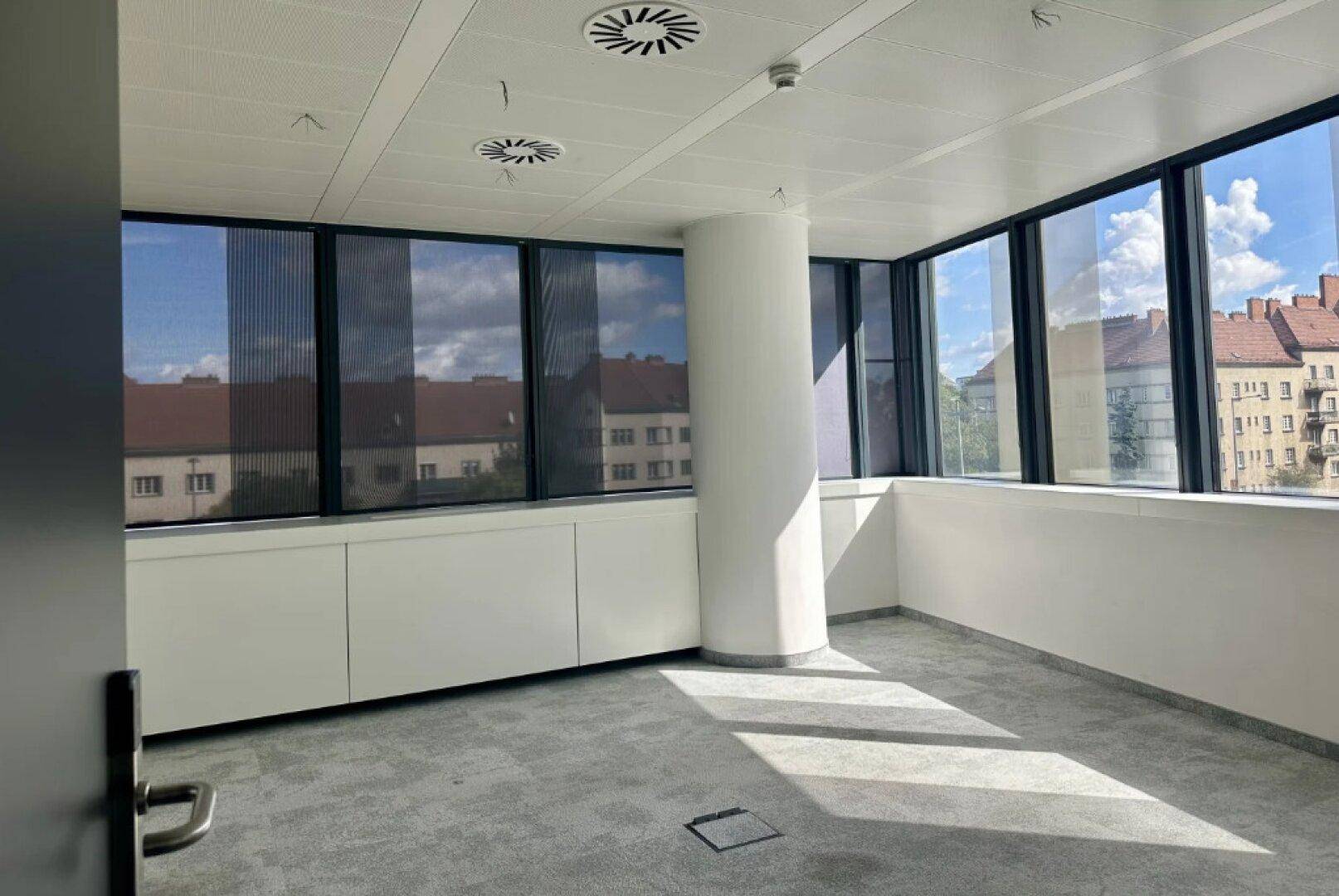 Geräumiges Büro mit großen Fenstern, die viel Tageslicht hereinlassen, und einem modernen Teppichboden.