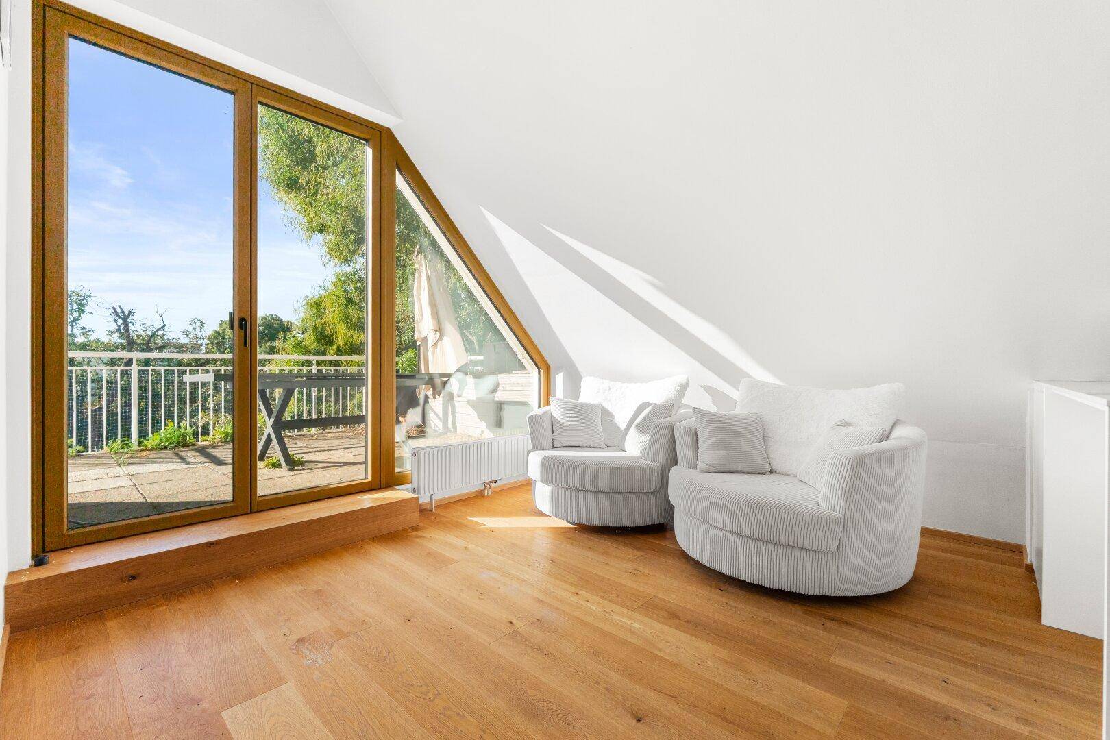 Gemütlicher Sitzbereich mit zwei Sesseln, Holzboden und großen Fenstern mit Terrassenzugang.