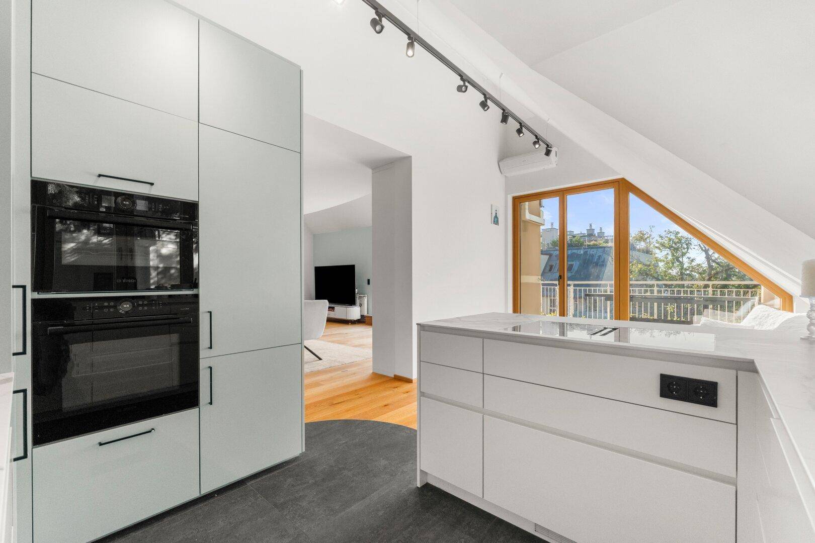 Helle Küche mit integrierten Backöfen, weißen Schränken und Blick in den Wohnbereich.