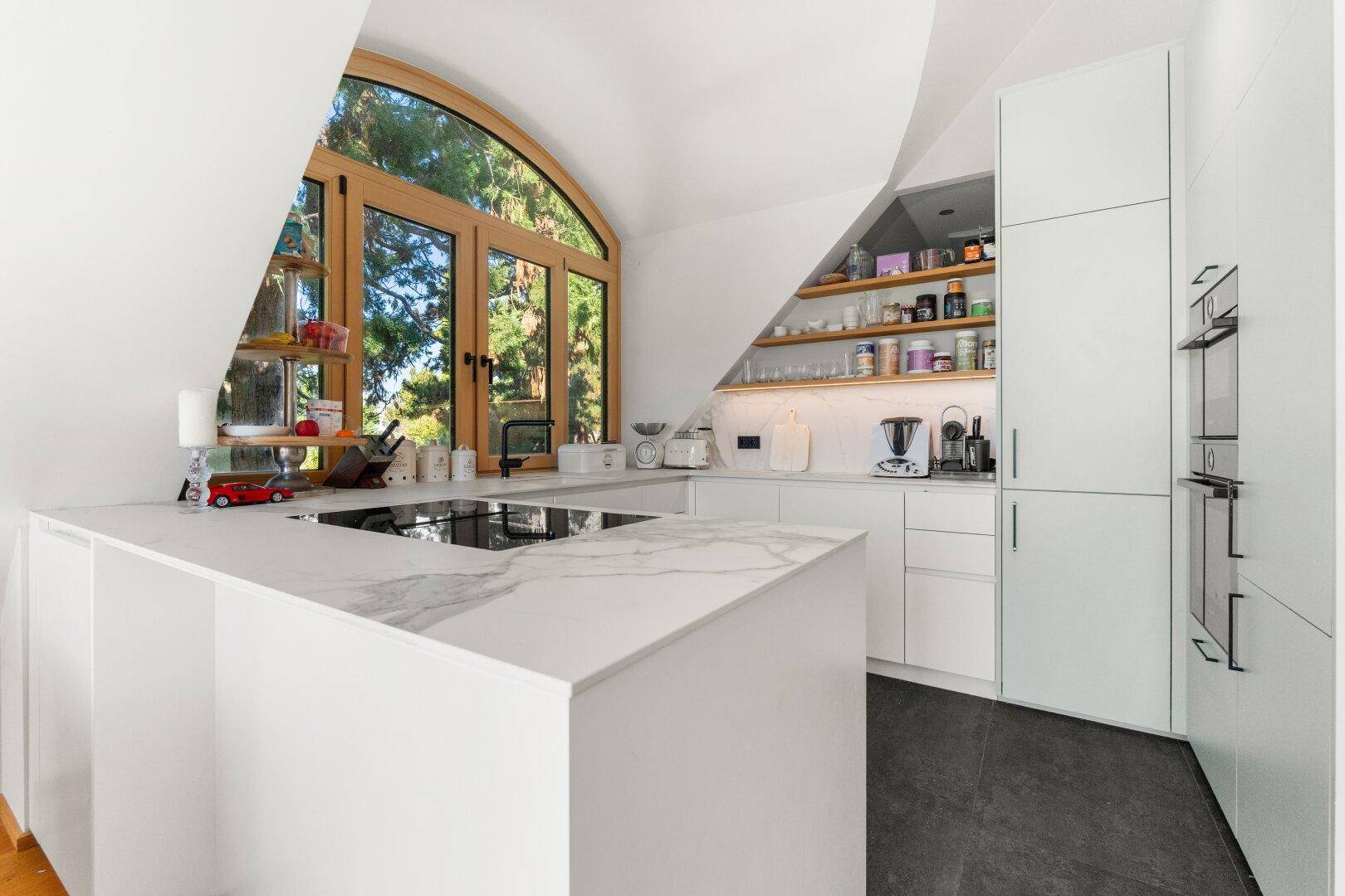 Moderne weiße Küche mit Kochinsel, Einbaugeräten und einem großen Bogenfenster.