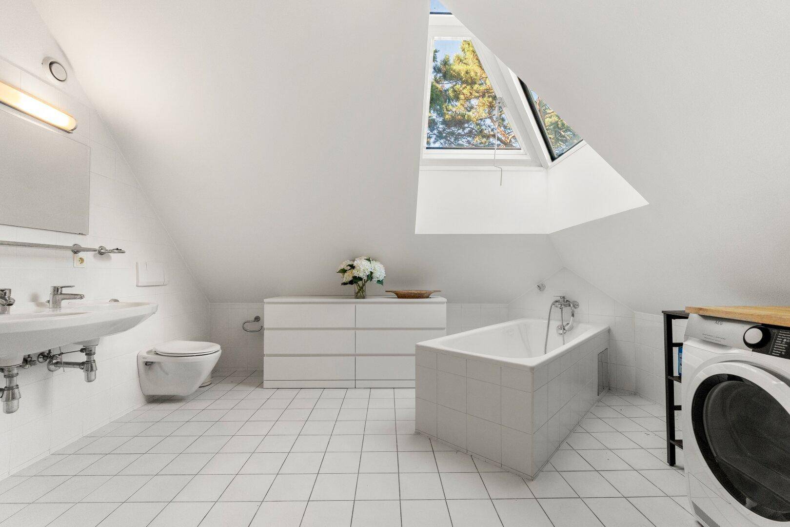 Helles Badezimmer mit Badewanne, Waschbecken, WC und Dachfenster im Dachgeschoss.