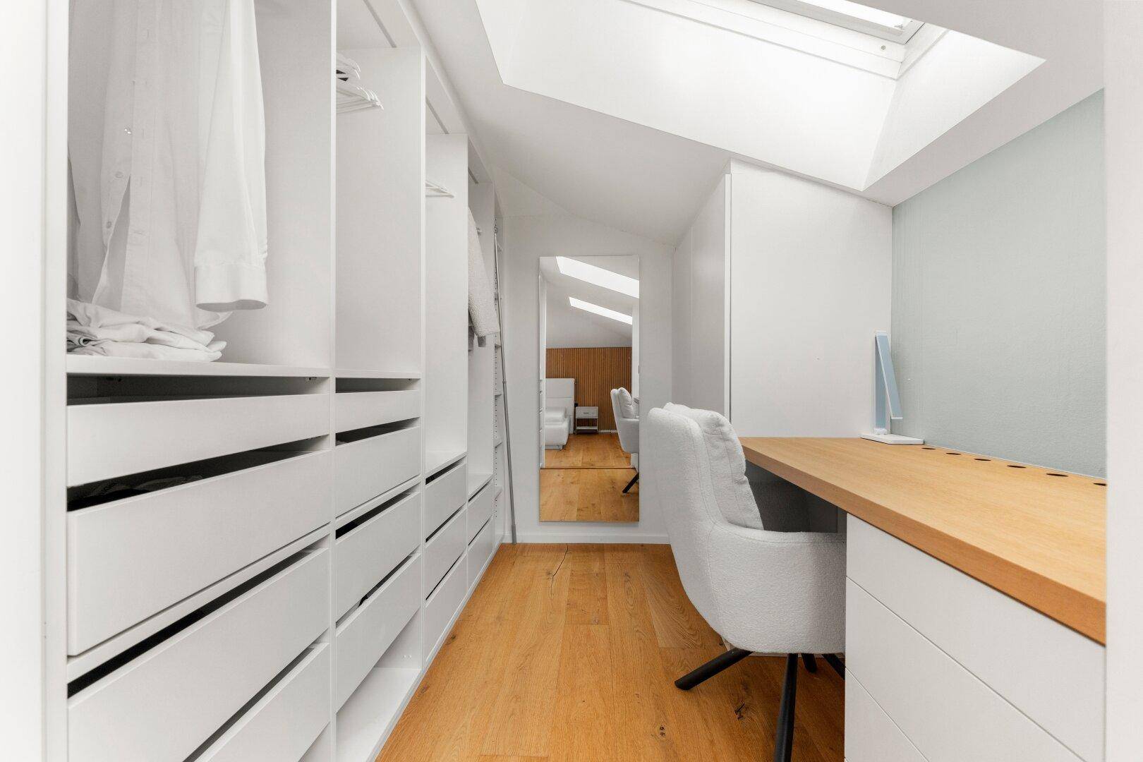 Begehbarer Kleiderschrank mit Einbauschränken, Schreibtisch und Dachfenster.