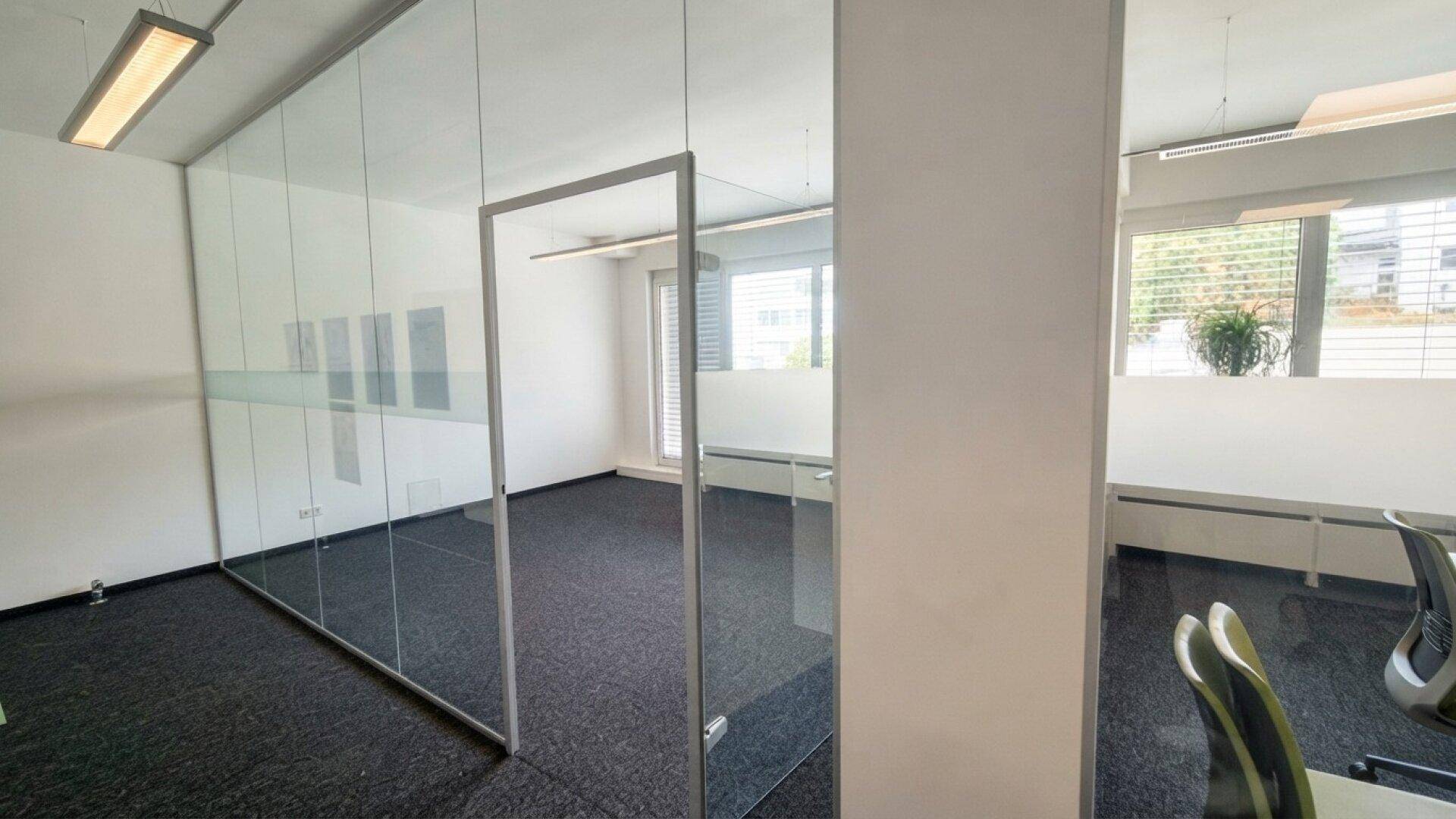Modernes Büro mit Glaswänden, dunklem Teppichboden und klaren Linien, das eine offene Arbeitsatmosphäre schafft.