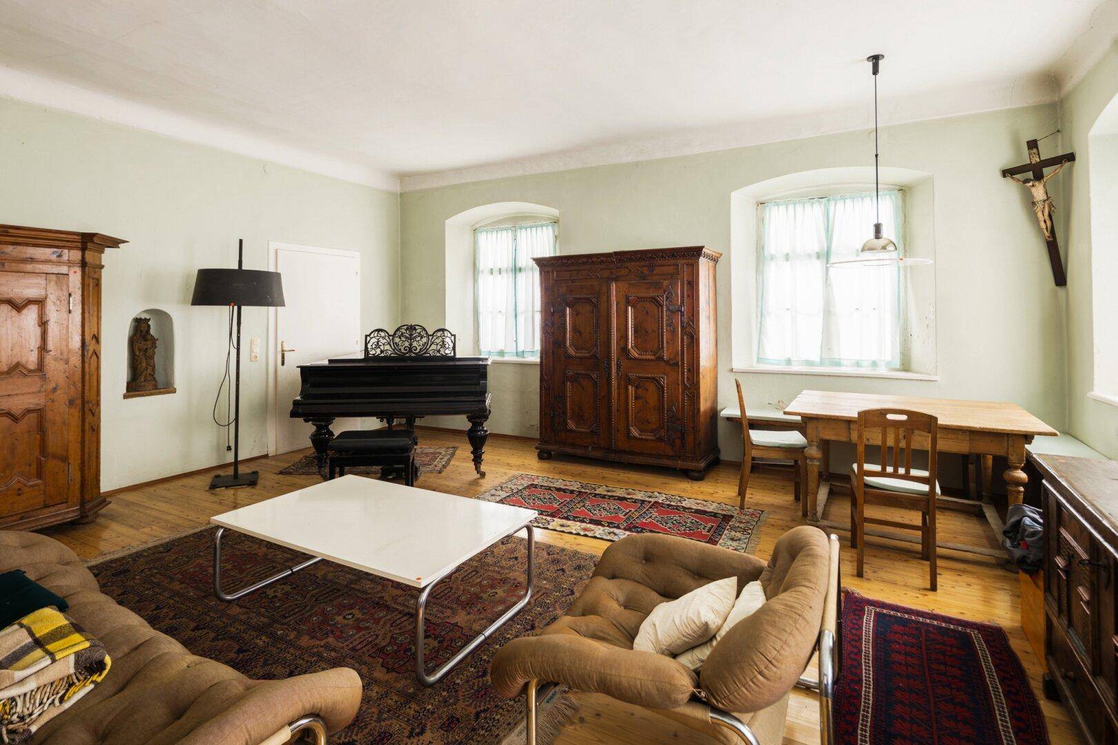 Geräumiges Wohnzimmer mit Holzboden, antiken Möbeln, Teppichen und einem Flügel.