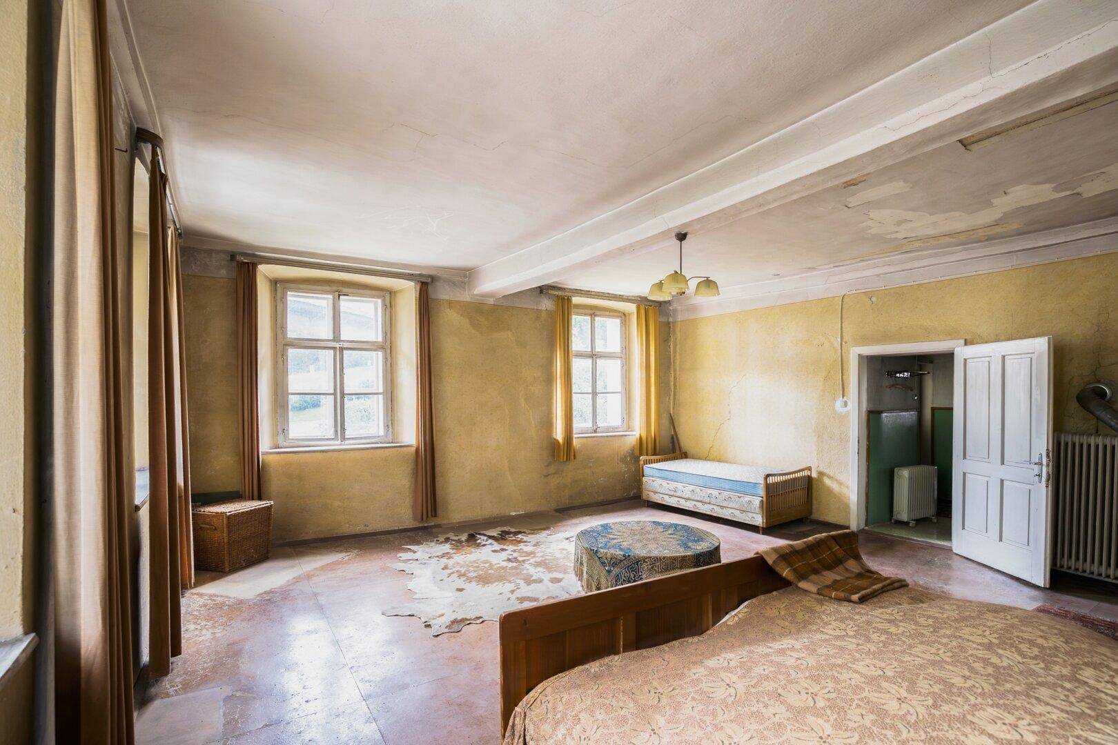 Geräumiges Schlafzimmer mit renovierungsbedürftigen Wänden, traditionellem Bett und Fenstern.