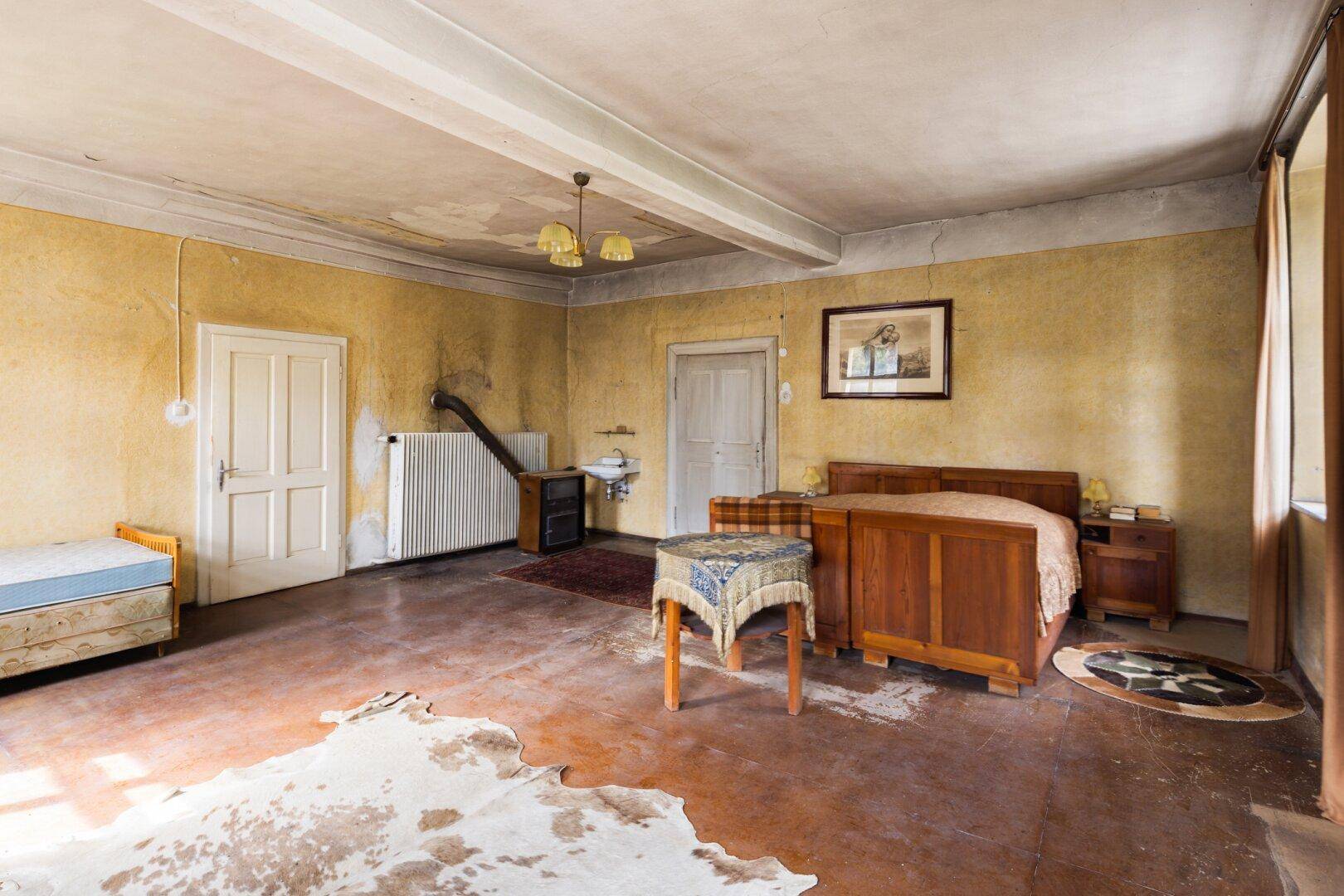 Schlafzimmer mit traditionellem Bett, Heizkörper und Spuren der Zeit an den Wänden.
