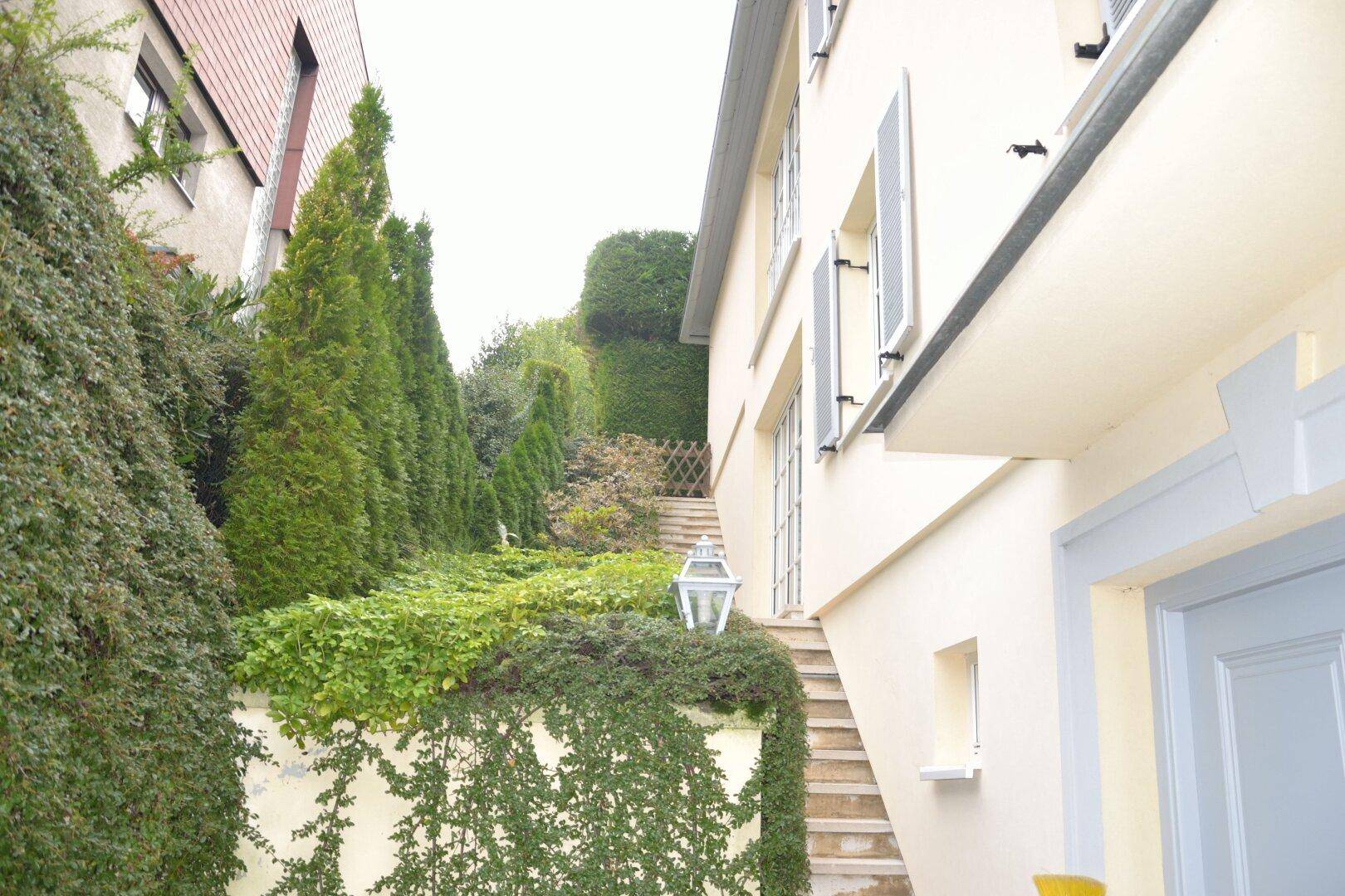 Seitlicher Gartenbereich mit Treppe, üppiger Bepflanzung und einer dekorativen Laterne.