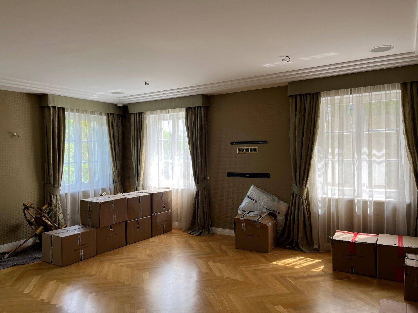 Geräumiges Wohnzimmer mit Fischgrätparkett, hohen Fenstern und Vorhängen.