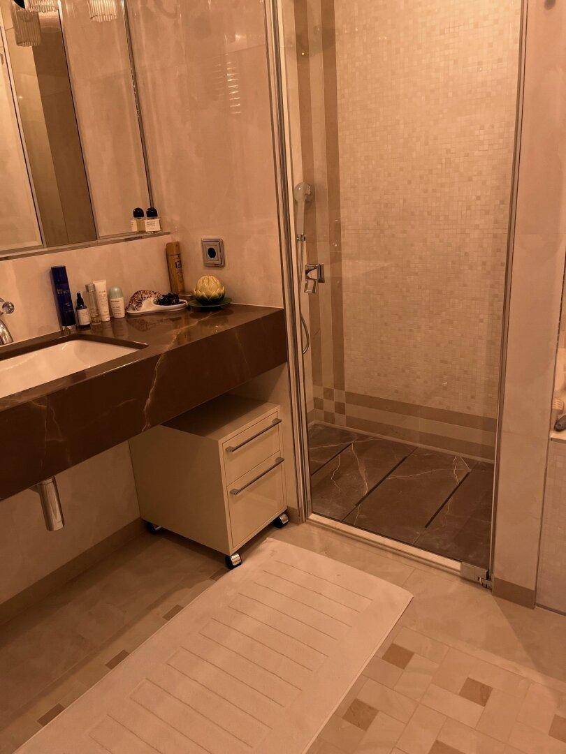 Modernes Badezimmer mit Marmorwaschtisch, begehbarer Dusche und hellen Fliesen.