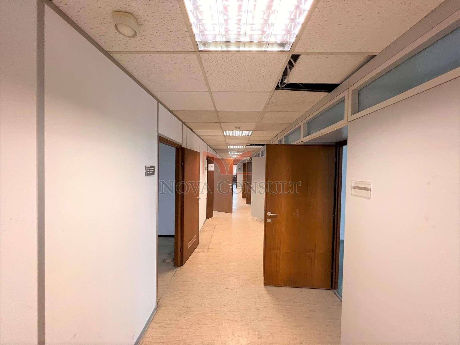 Langer Flur mit mehreren Holztüren, die zu verschiedenen Büros oder Räumen führen, mit abgehängter Decke.