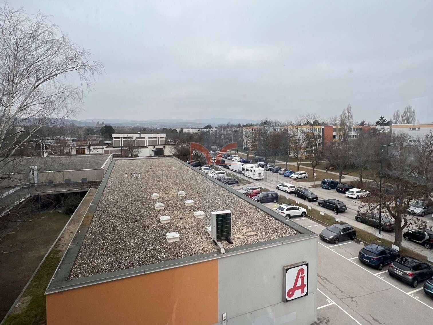 Panoramablick von oben auf ein Flachdach, einen großen Parkplatz und die umliegende Bebauung der Stadt.
