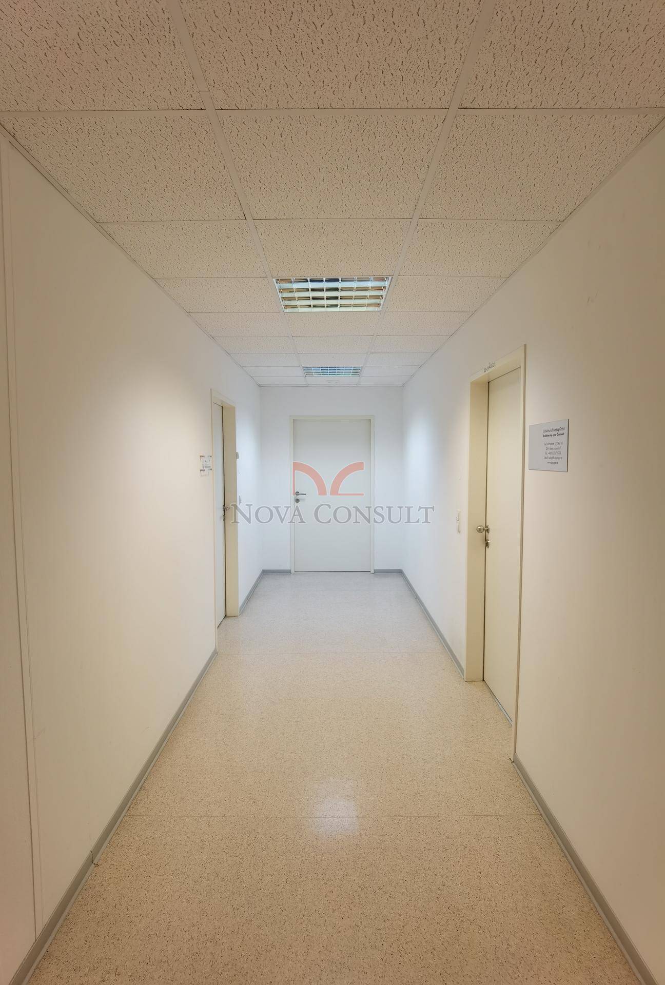 Langer, heller Flur mit hellem Fliesenboden und mehreren Türen, der verschiedene Büroräume verbindet.
