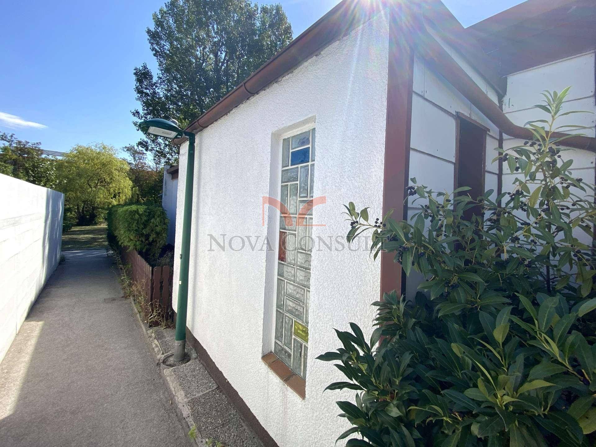 Ecke des Hauses mit einem schmalen Fenster und umgebenden Büschen unter hellem Sonnenlicht.