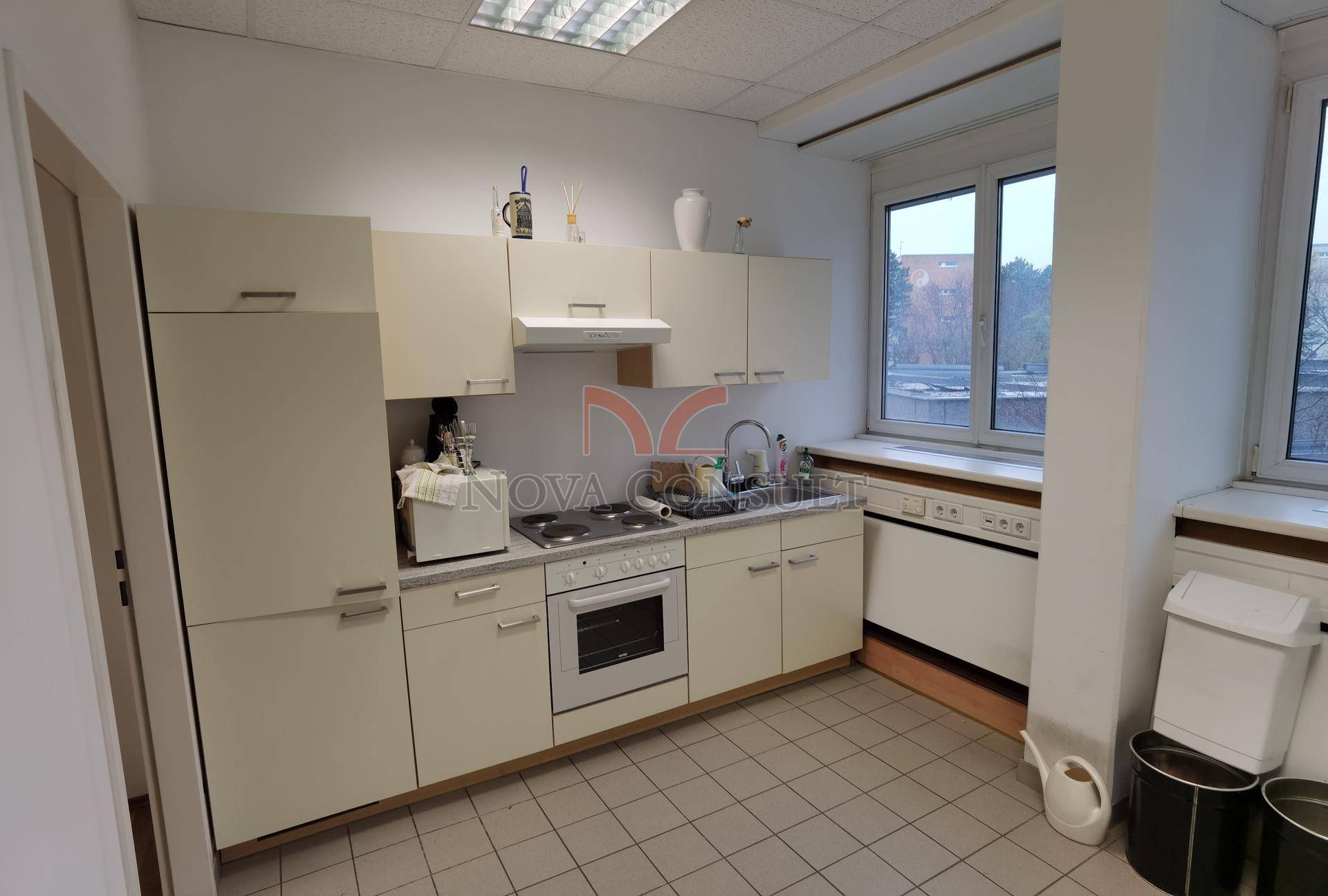 Funktionale Küche mit beigefarbenen Schränken, Fliesenboden und einem Fenster mit Blick nach draußen.