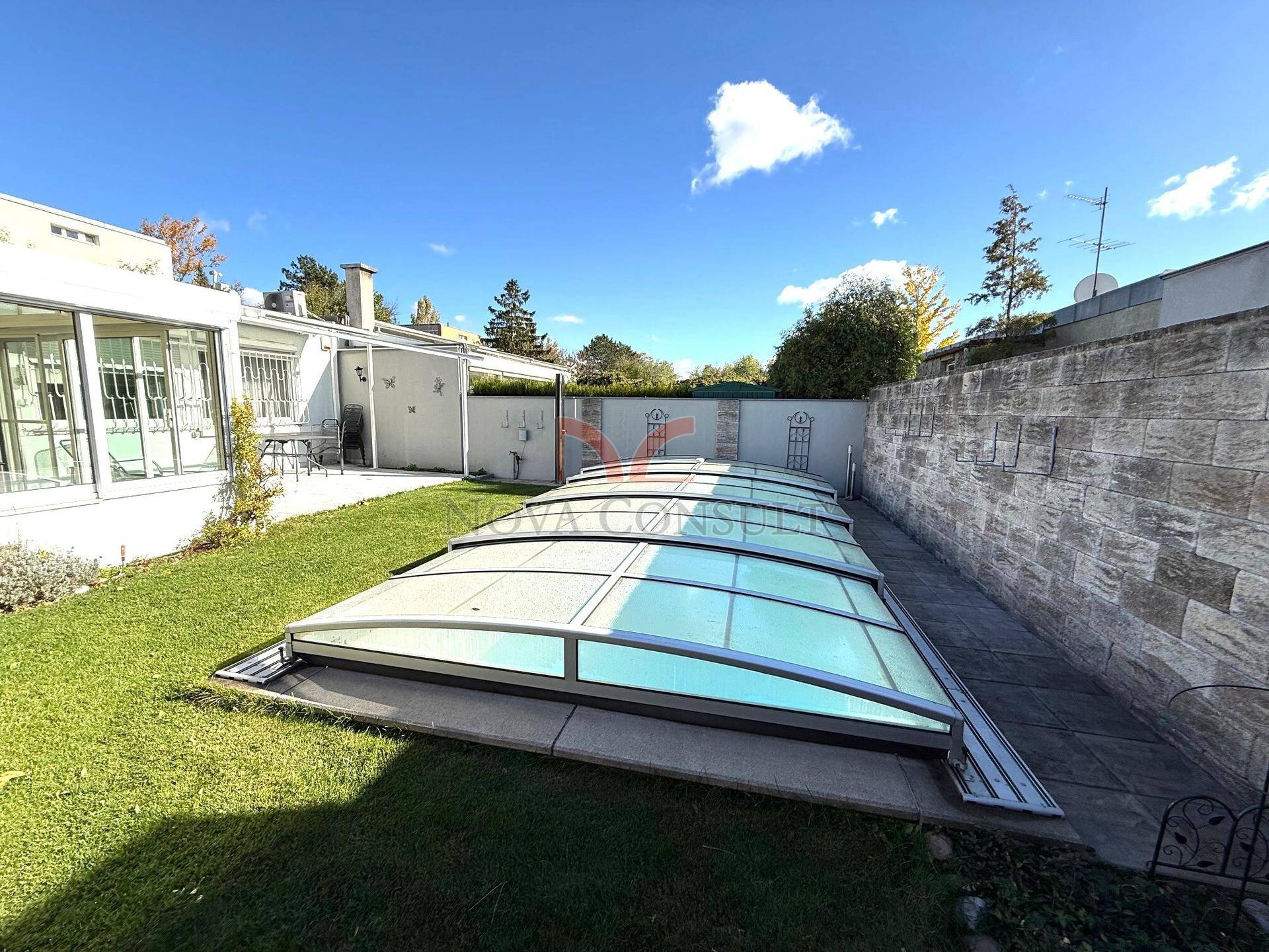 Weitläufiger Gartenbereich mit großem, überdachtem Pool und einer Steinmauer im Hintergrund.
