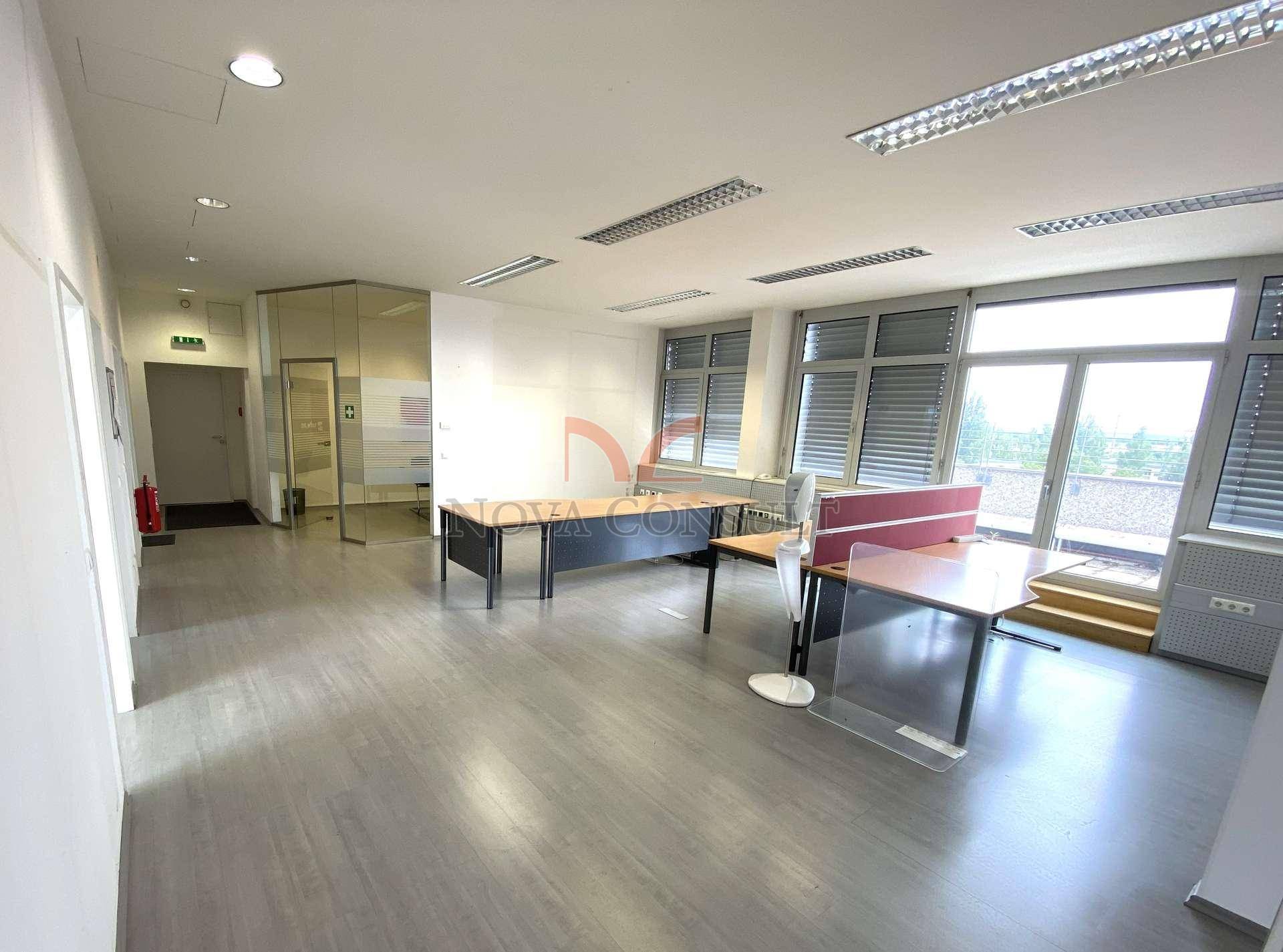 Helles und geräumiges Büro mit großen Fenstern, modernen Leuchten und Zugang zu einem Außenbereich.