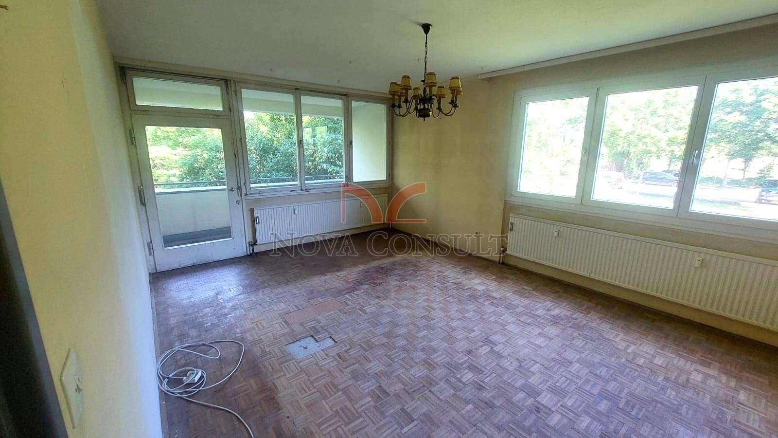Helles Zimmer mit Parkettboden, Kronleuchter und Zugang zu einem Balkon.