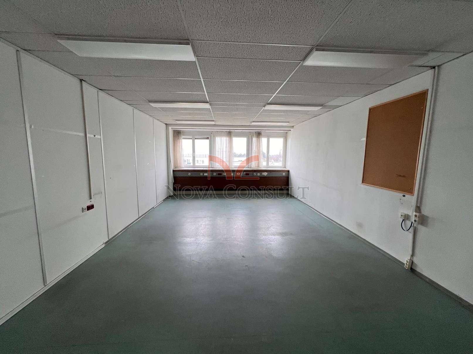 Langes, leeres Büro mit vielen Fenstern am Ende des Raumes und einer abgehängten Decke.