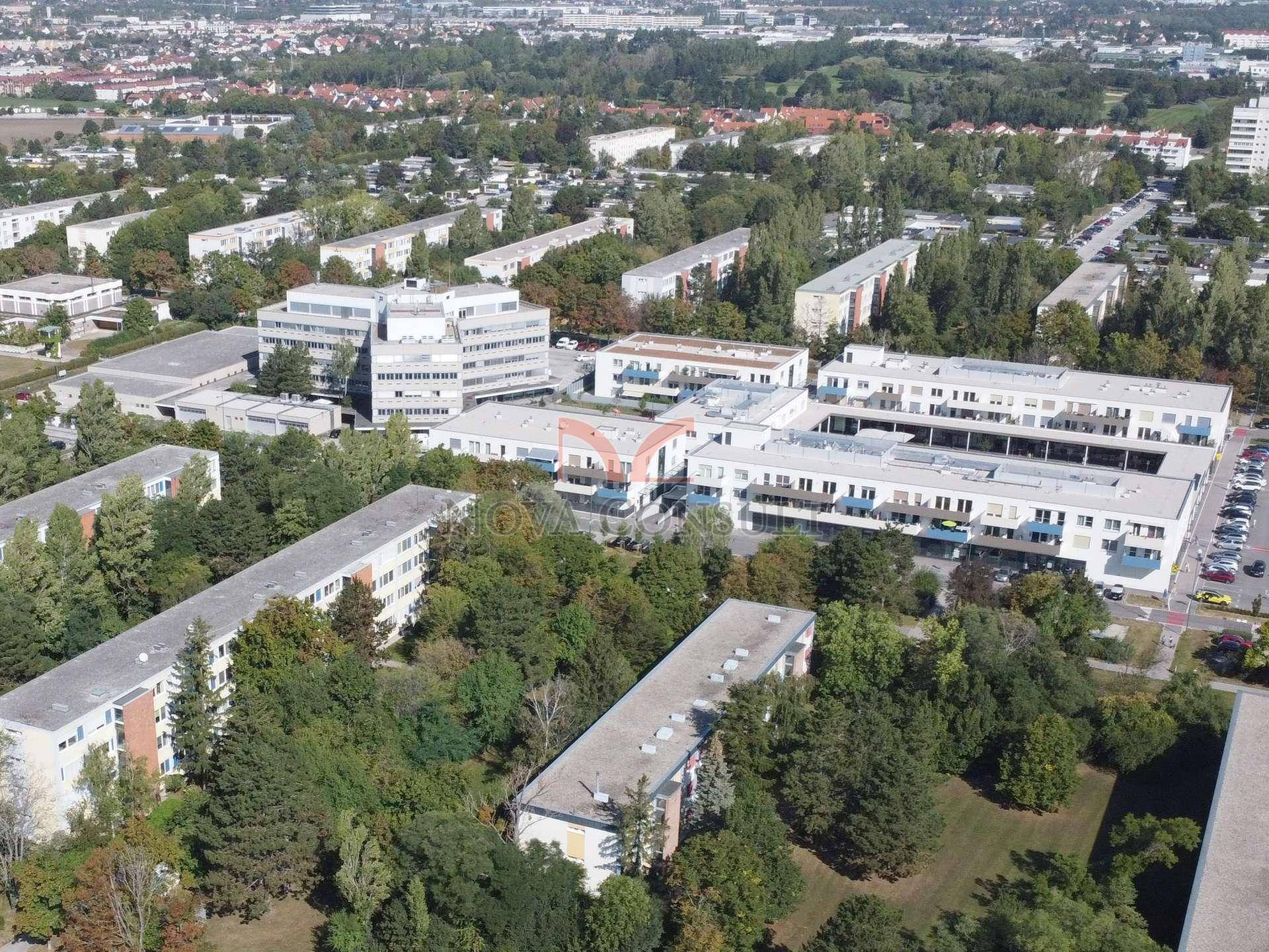 Luftaufnahme eines großen Gebäudekomplexes umgeben von viel Grün und weiteren Wohngebäuden.